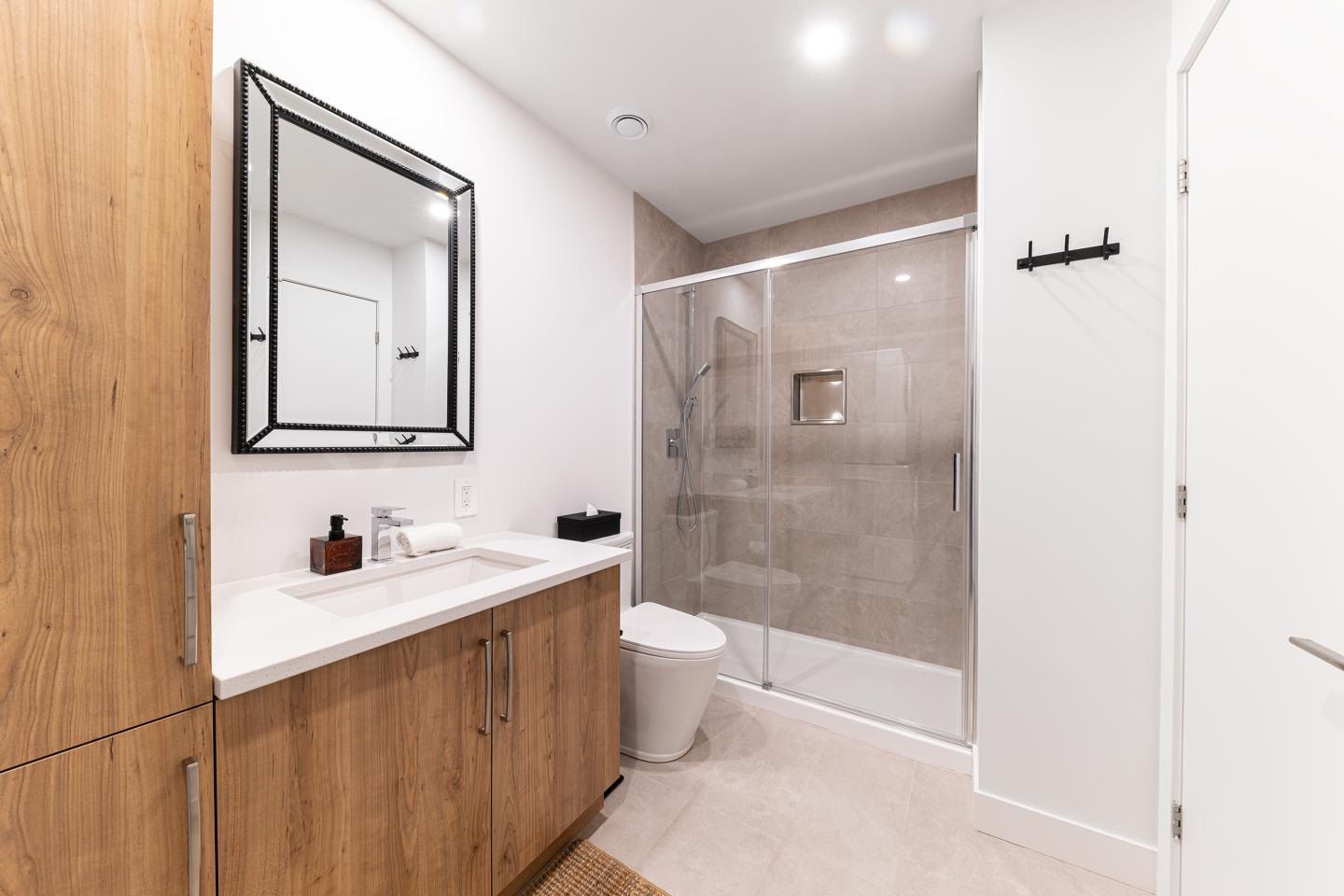 Salle de bain moderne avec douche vitrée, meuble en bois et miroir rectangulaire.