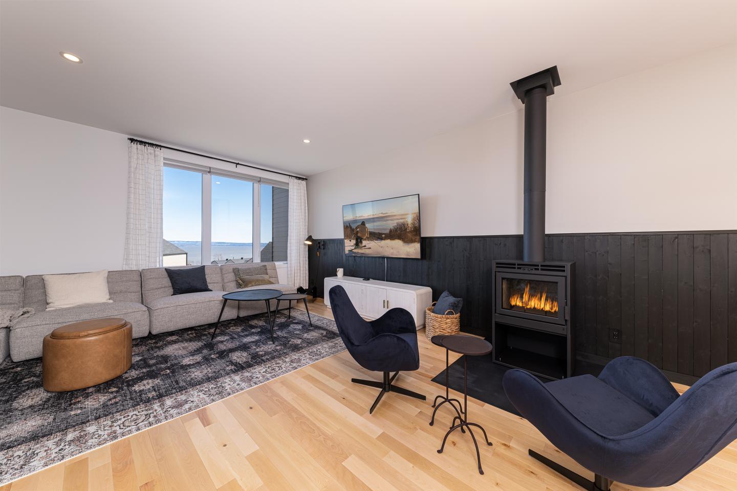 Salon moderne avec poêle à bois, canapé gris, et fauteuils bleus.