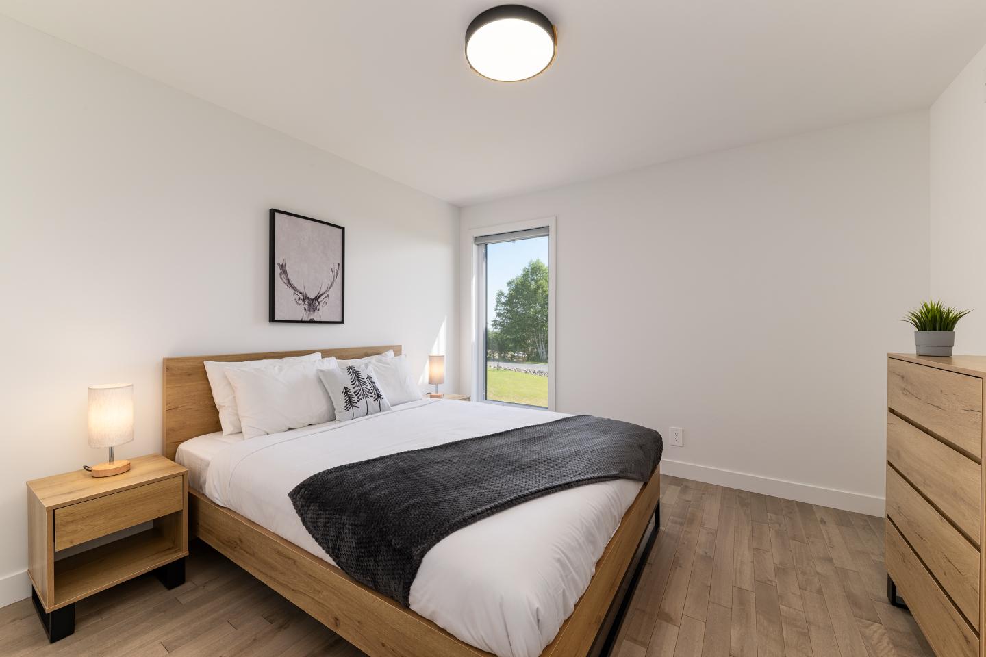 Chambre moderne avec lit double, lumière naturelle, commode et plantes.