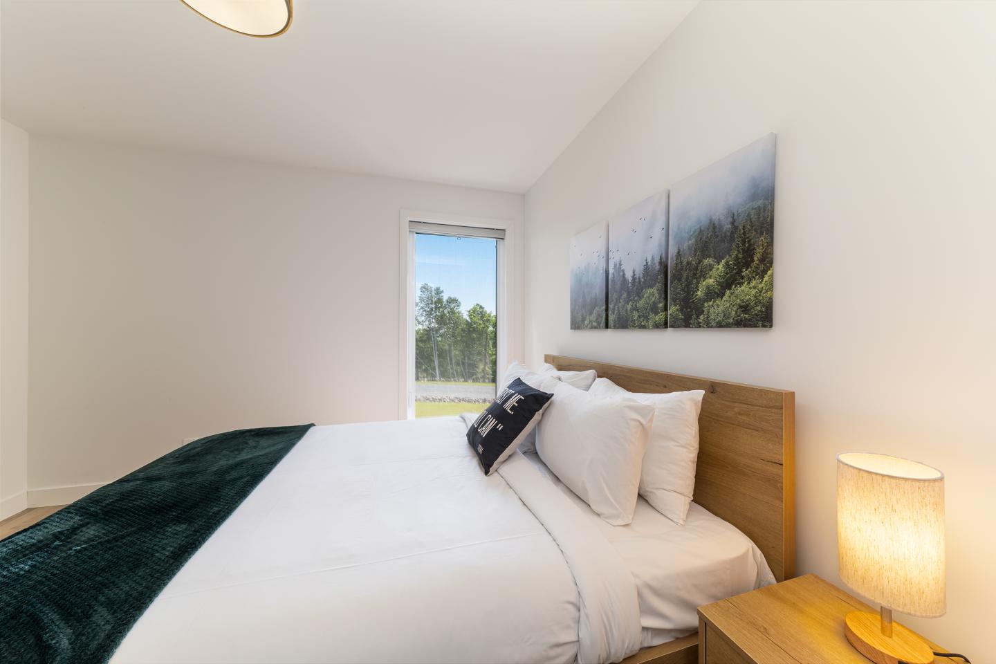 Chambre moderne lumineuse avec lit double, lampe, et tableau mural.