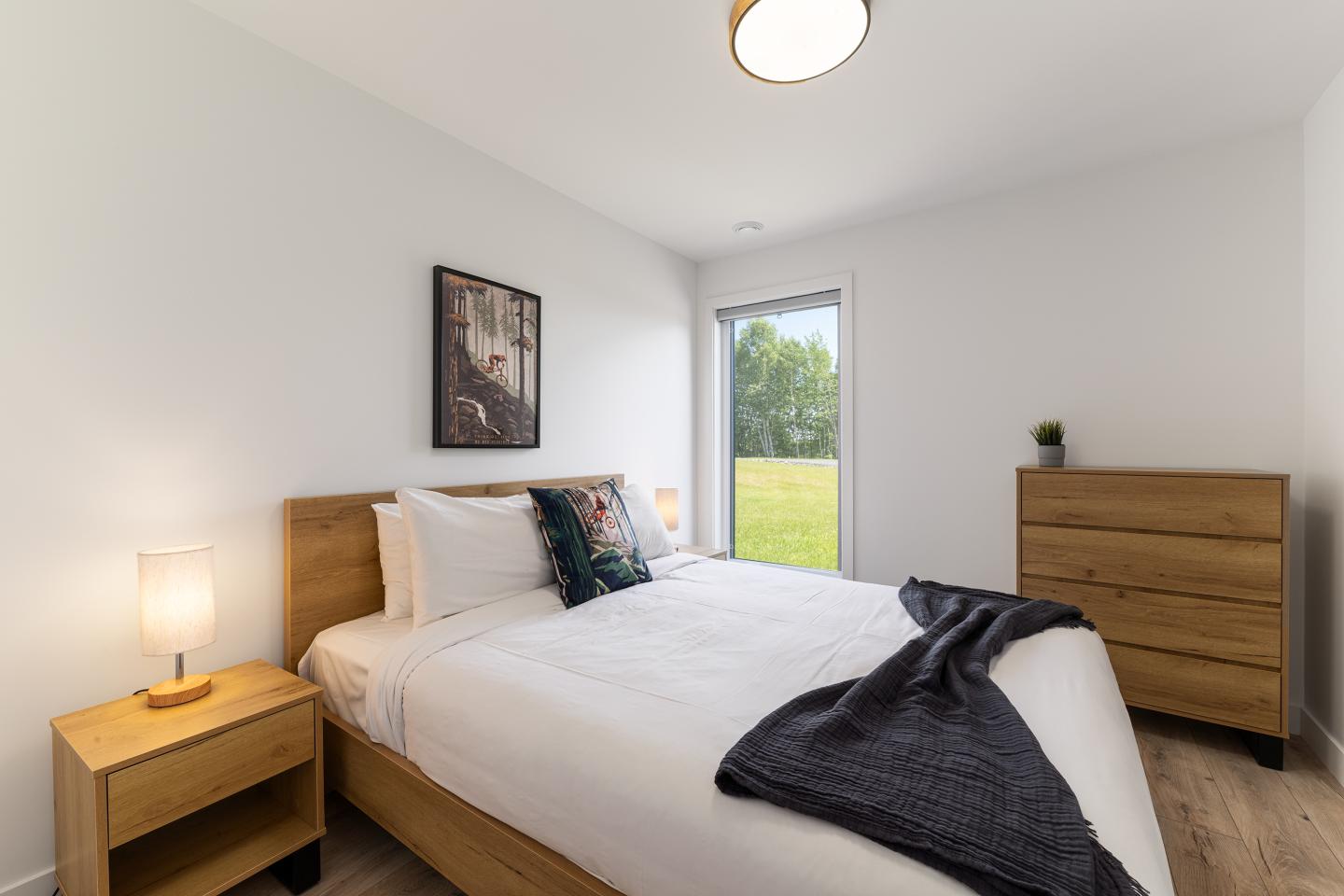 Chambre moderne avec lit double, commode et fenêtre donnant sur jardin.
