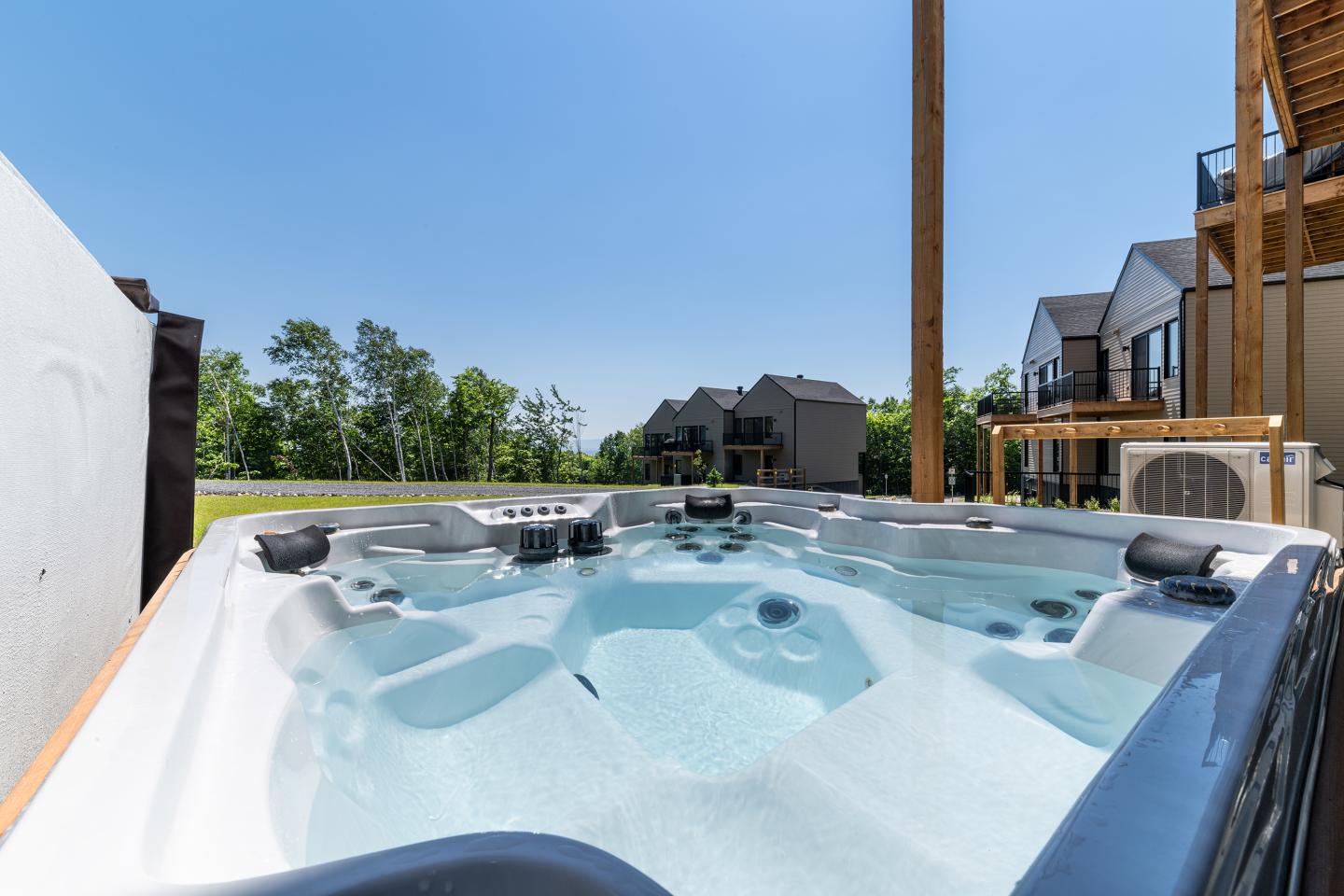 Jacuzzi extérieur sous un ciel bleu, maisons en arrière-plan.