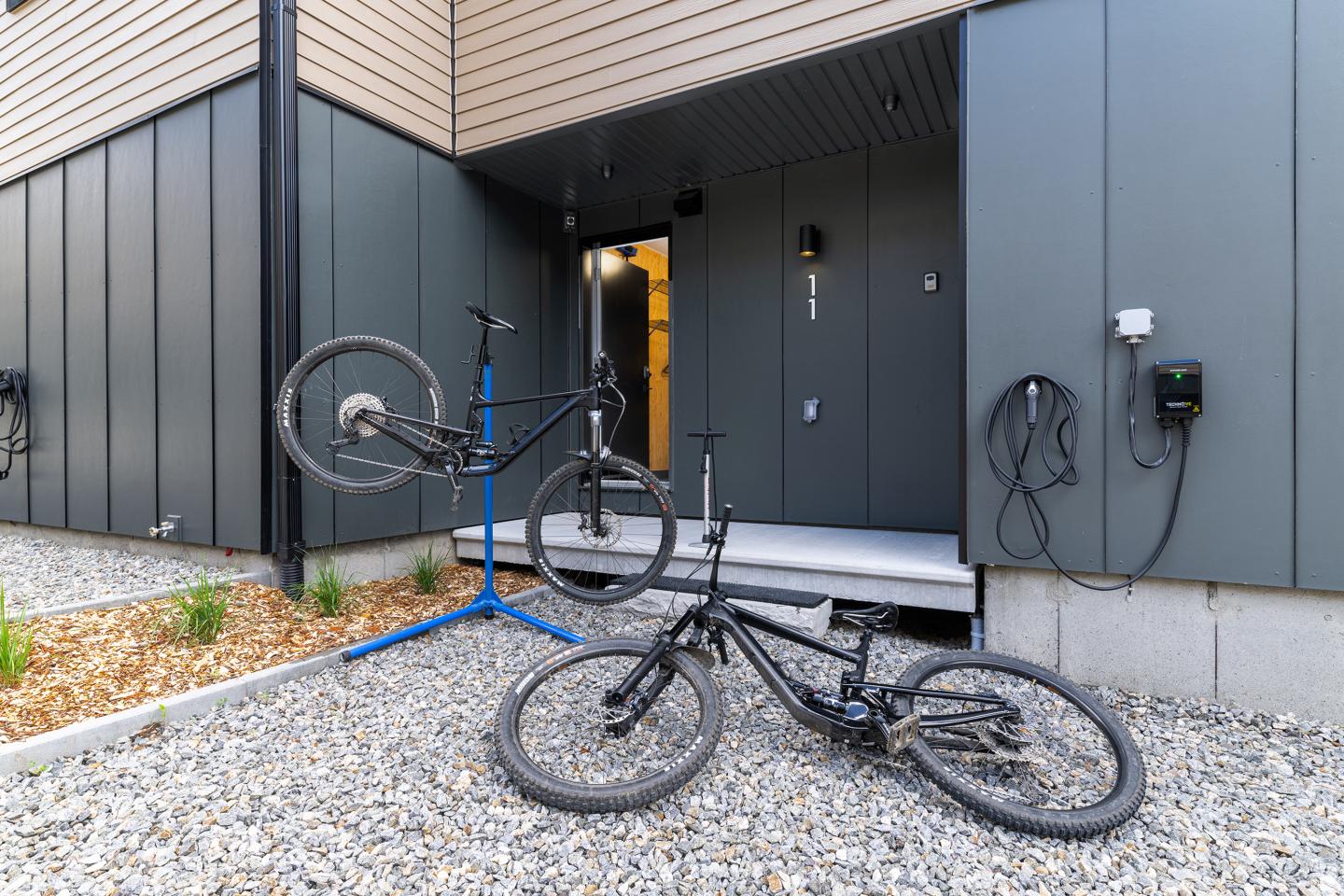 Deux vélos devant une entrée moderne, l'un sur un pied d'atelier, l'autre par terre.