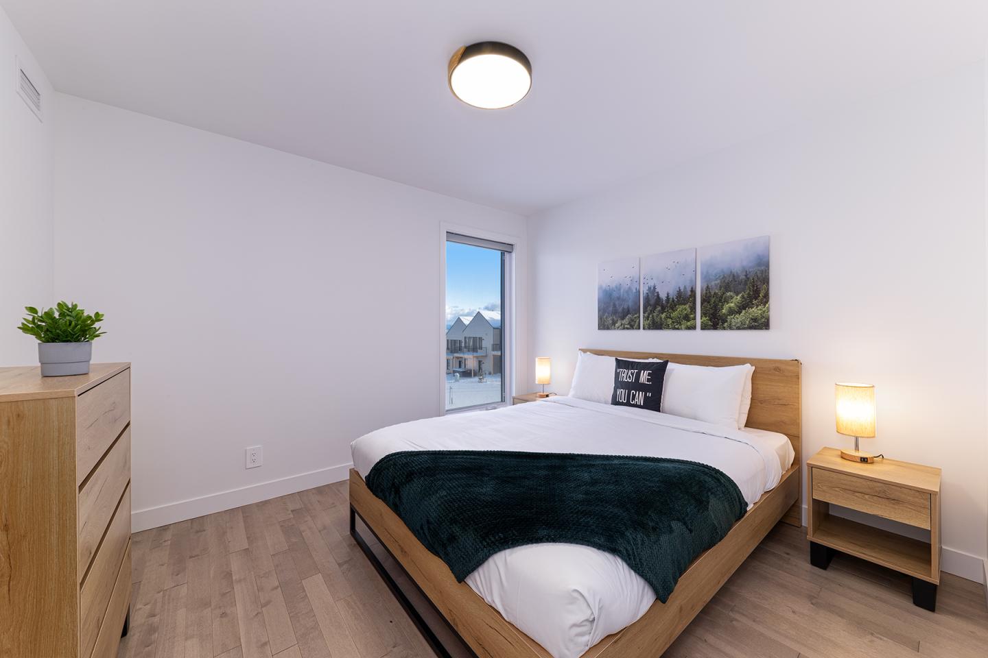 Chambre moderne avec lit double, tableau mural, et lumière naturelle.