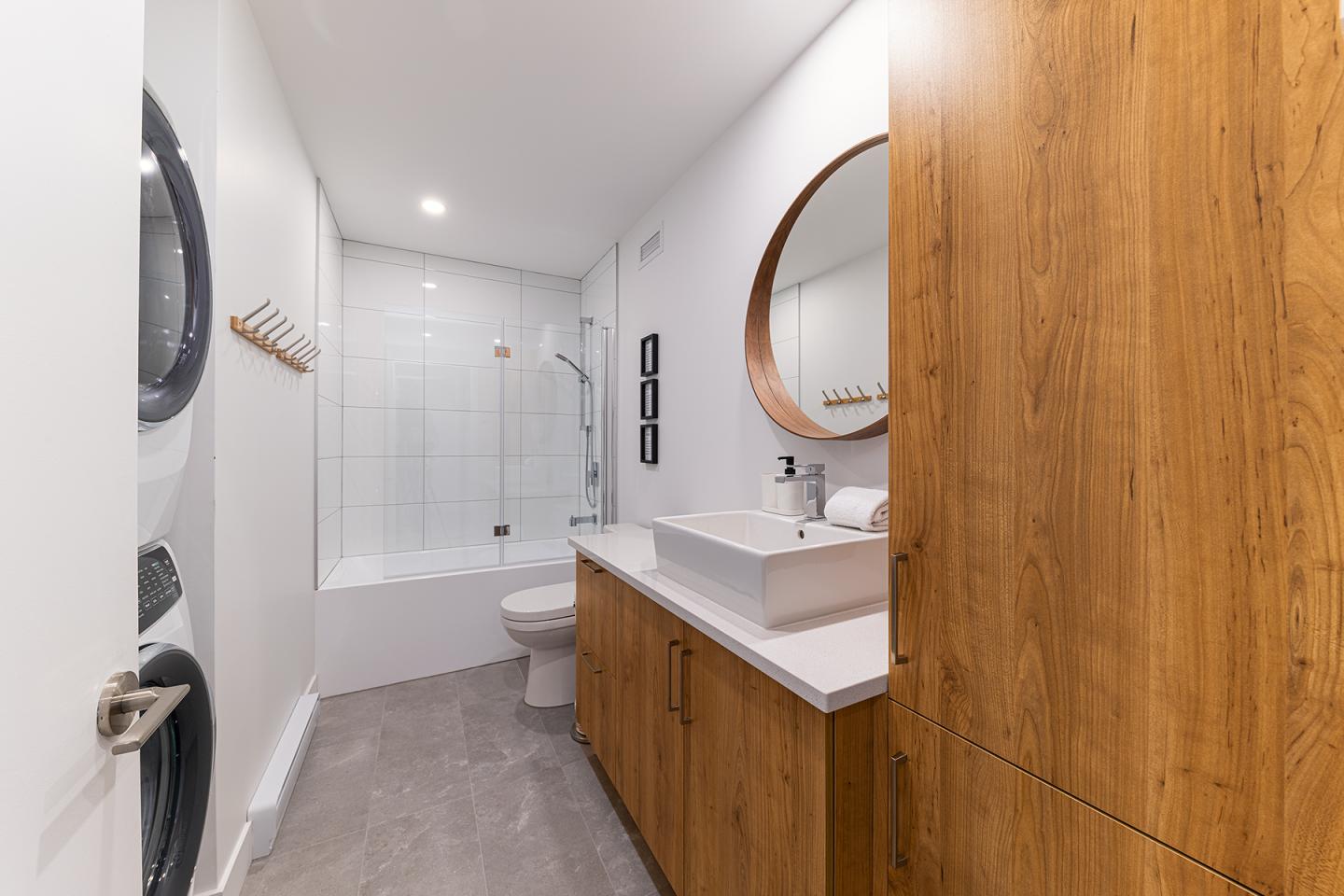 Salle de bain moderne avec lavabo en bois, miroir rond et douche vitrée.