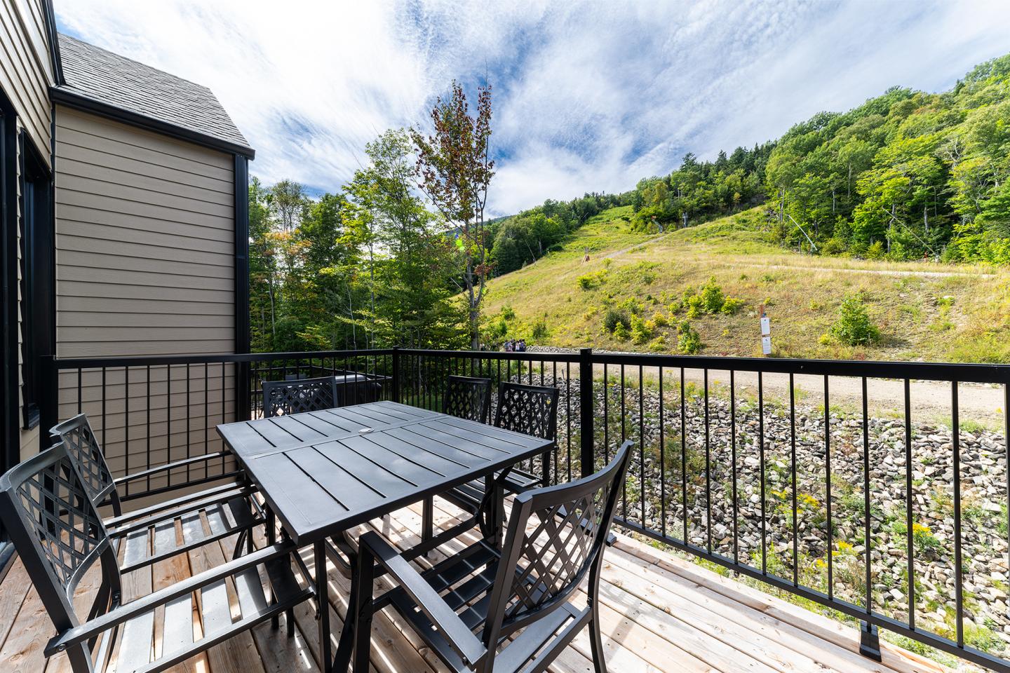 Terrasse avec table et chaises sur fond de colline verdoyante et ciel bleu.