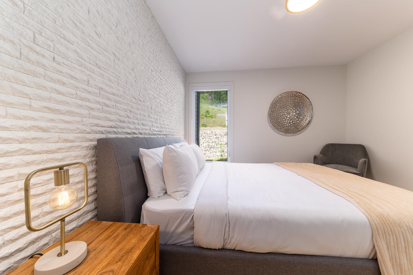 Chambre moderne avec mur de briques, lit double et lampe en bois.