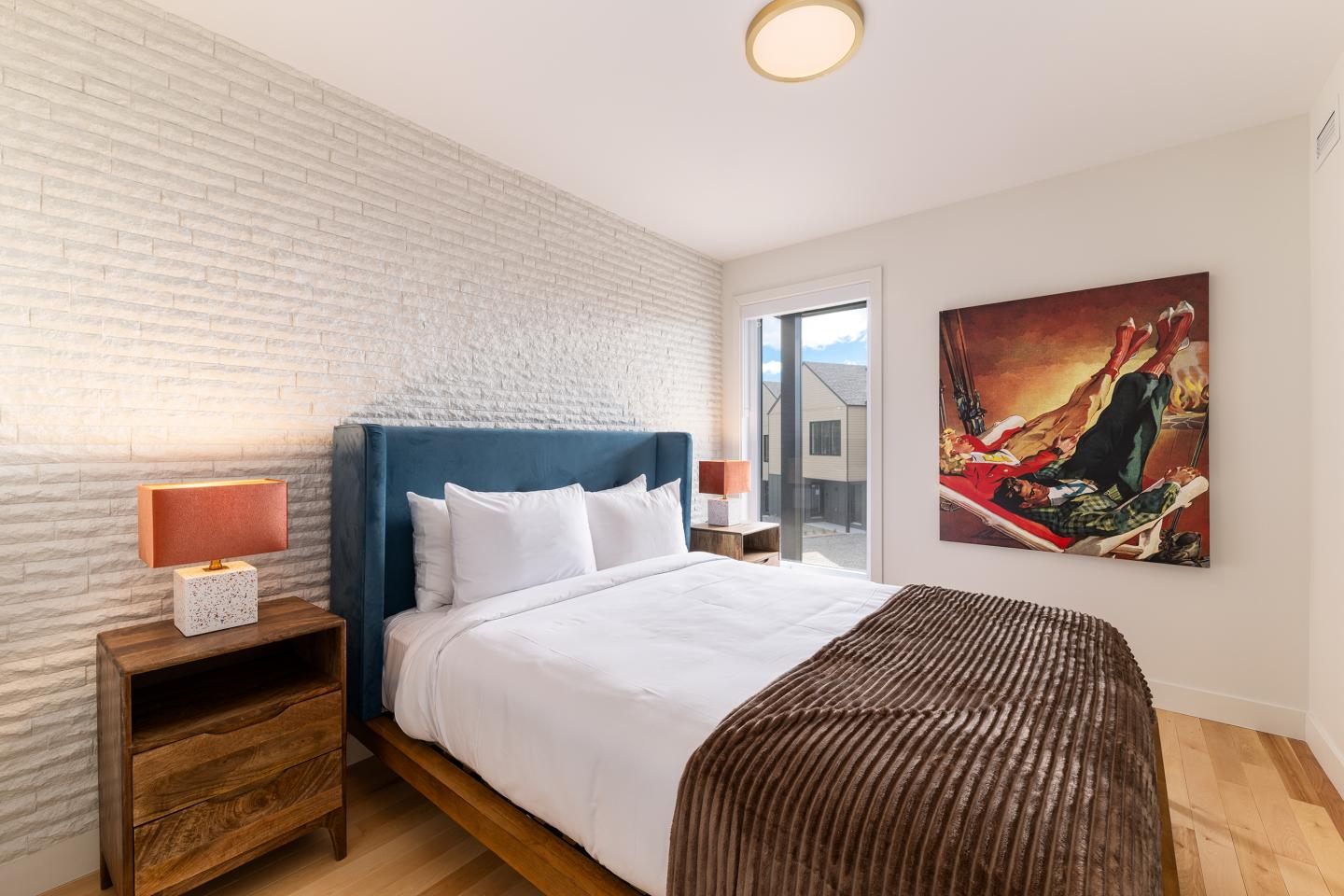 Chambre moderne avec lit double, lampes de chevet et tableau coloré au mur.