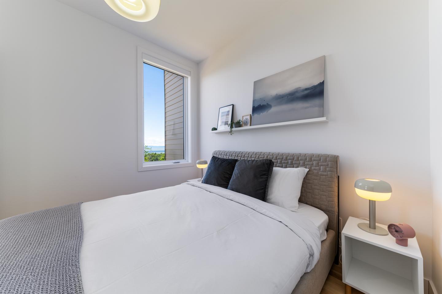 Chambre lumineuse avec lit double, fenêtre, lampes de chevet et tableau mural.