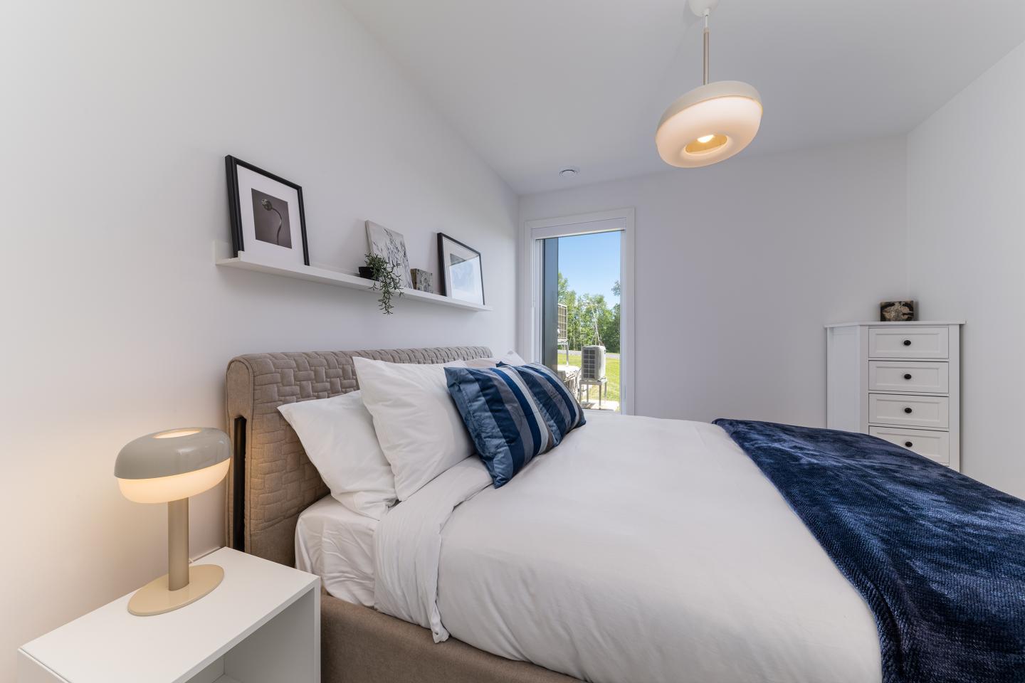 Chambre moderne avec lit, coussins bleus, et lampe de chevet. Fenêtre lumineuse.