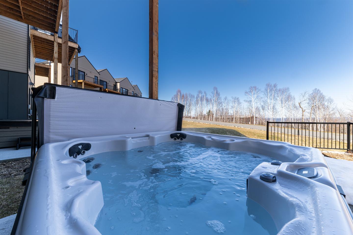 Spa extérieur bouillonnant sous ciel bleu près d'une maison.