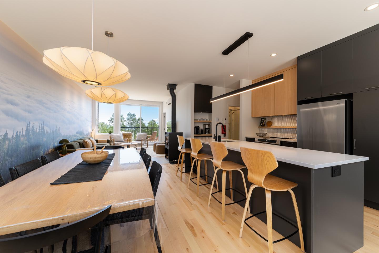 Cuisine moderne avec îlot, table à manger en bois, lampes suspendues.