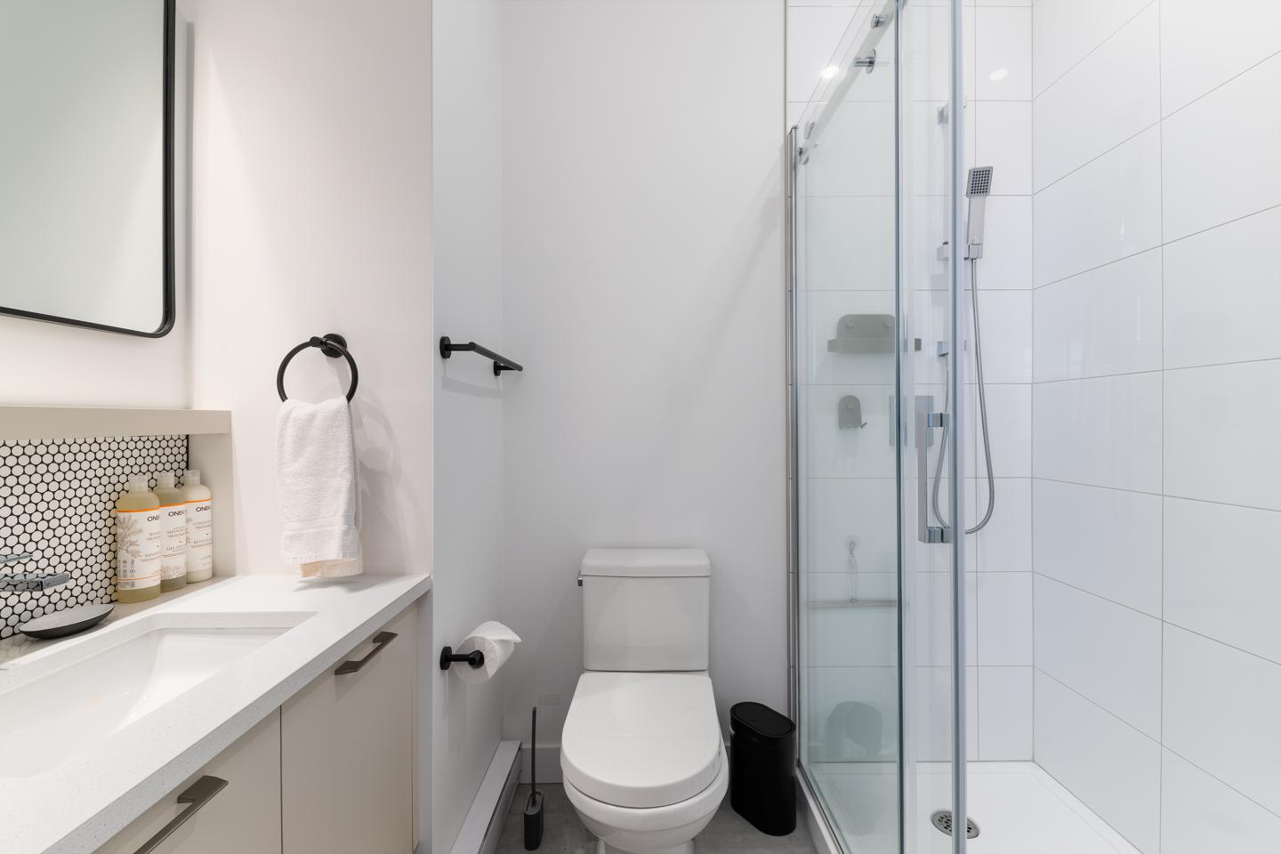 Salle de bain moderne avec douche vitrée, toilettes et lavabo blanc.