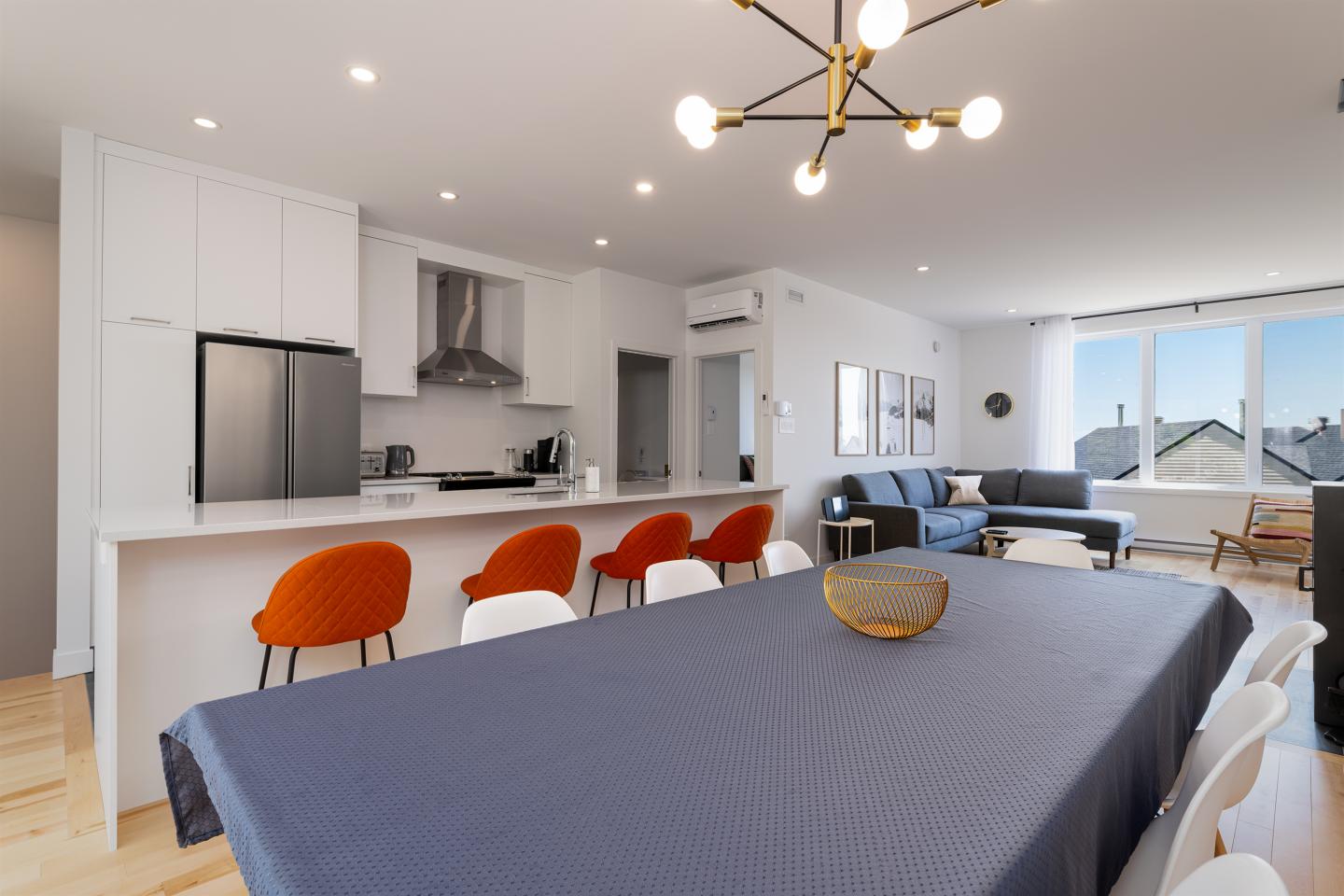 Salle à manger moderne avec table bleue, chaises rouges, et cuisine ouverte.