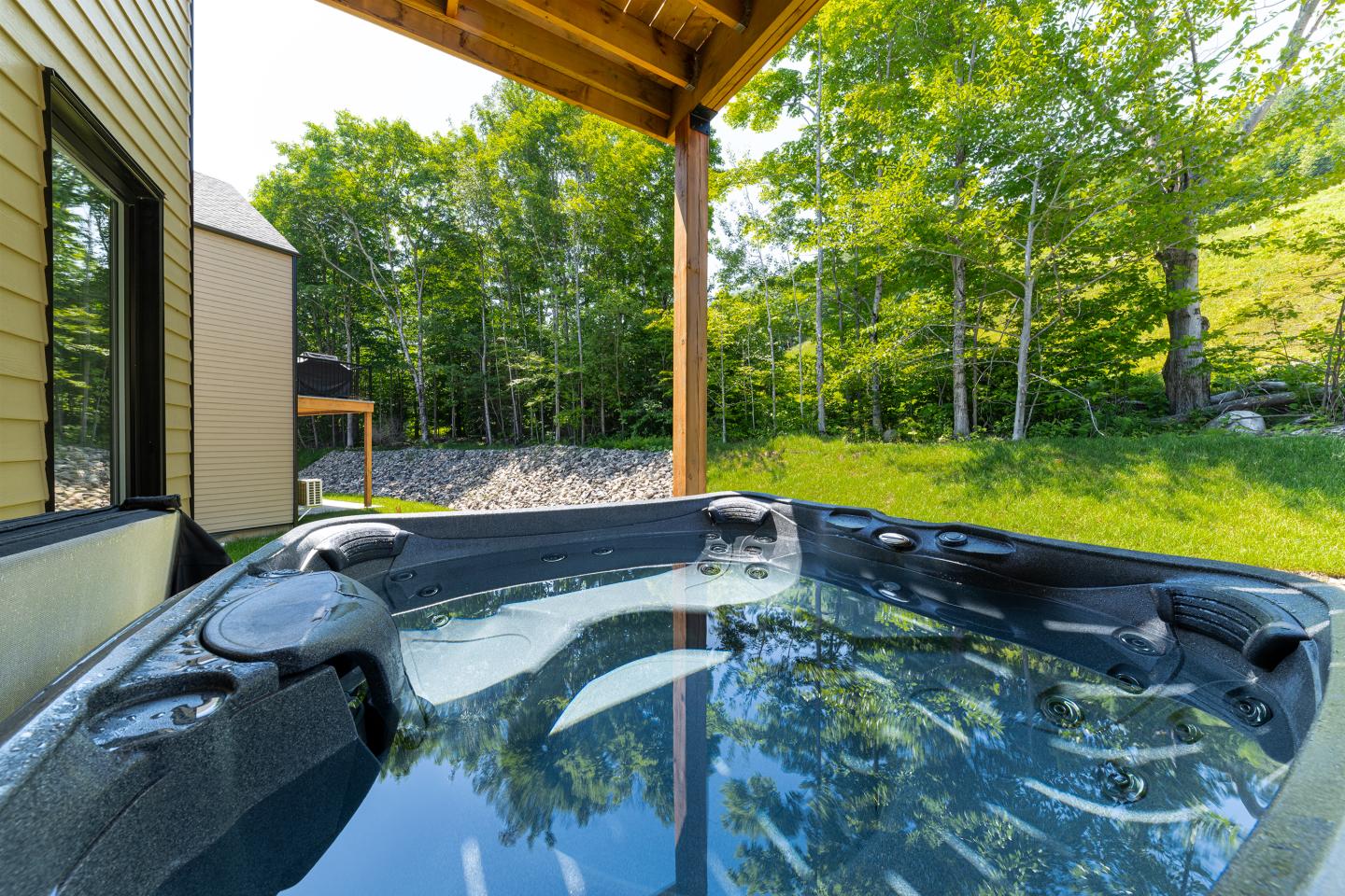 Spa extérieur sous abri en bois, entouré de verdure.