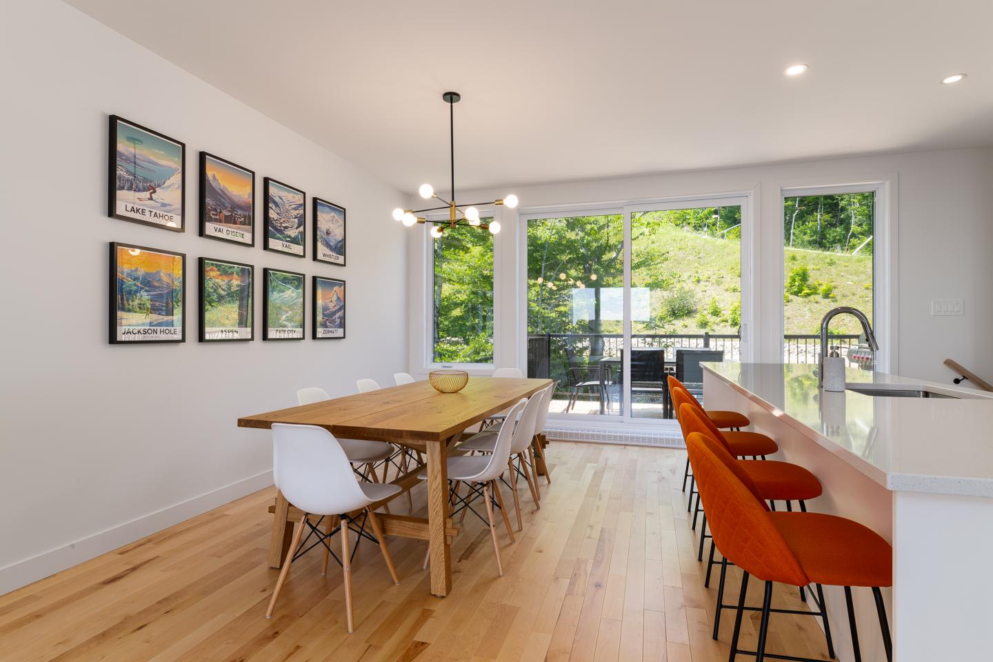 Salle à manger lumineuse avec table en bois, chaises blanches et fenêtres ouvertes sur jardin.
