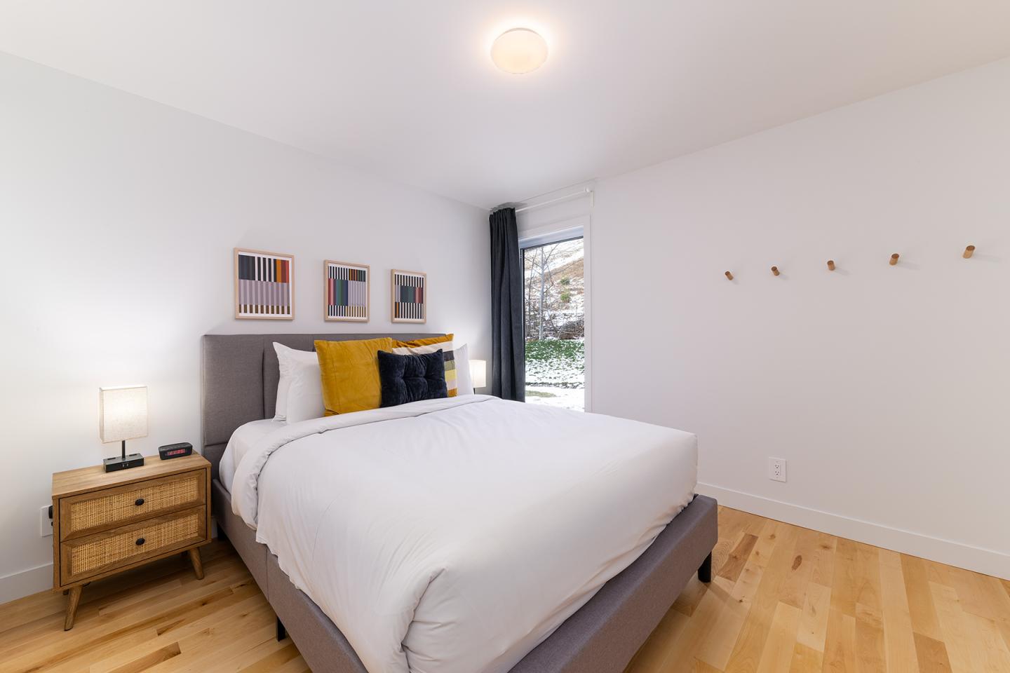 Chambre moderne, lit blanc avec coussins colorés, table de chevet en bois, lumière douce.