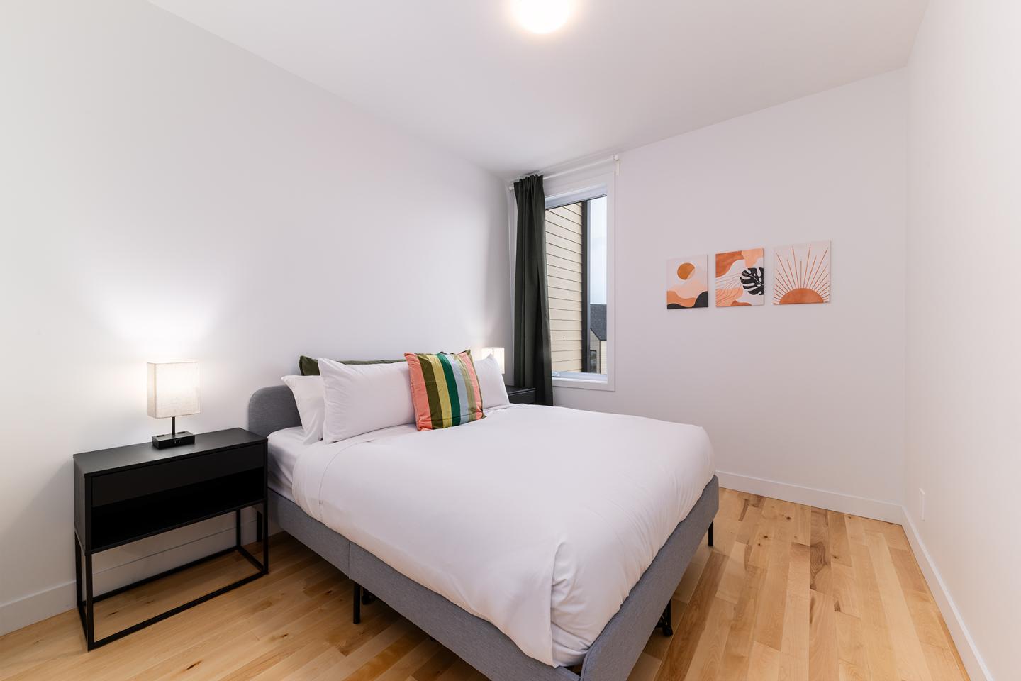 Chambre moderne avec lit double, oreillers colorés, table de chevet et lampadaire.
