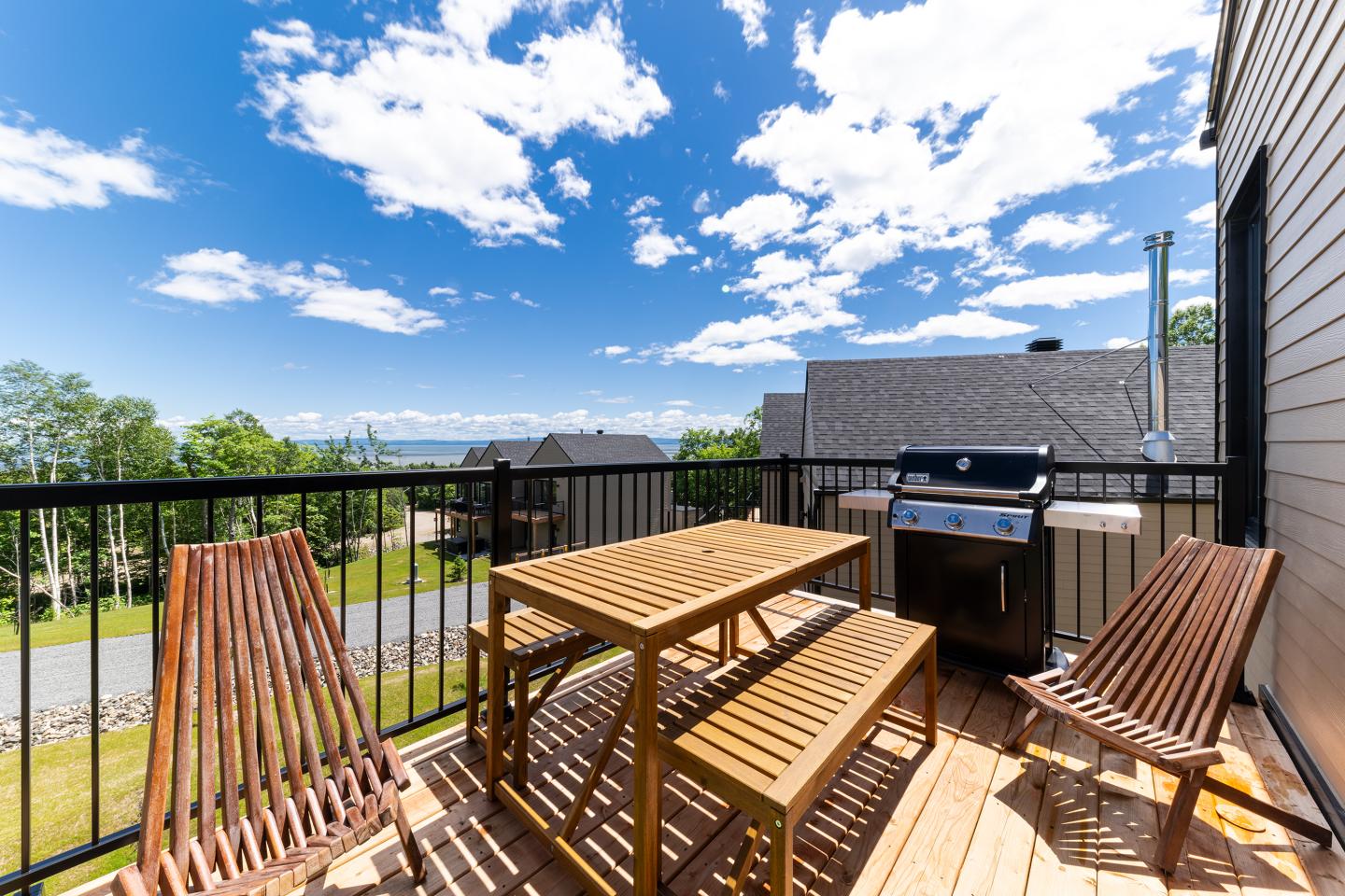 Terrasse ensoleillée avec table en bois, chaises et barbecue.