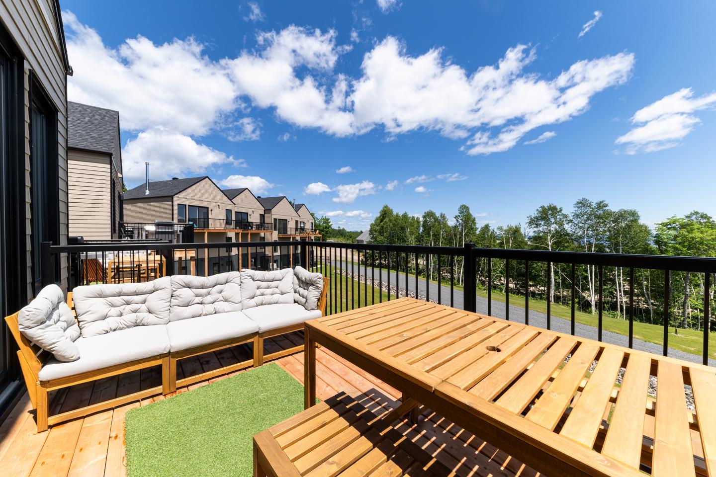 Terrasse ensoleillée avec canapé, table en bois, vue sur maisons et ciel bleu.