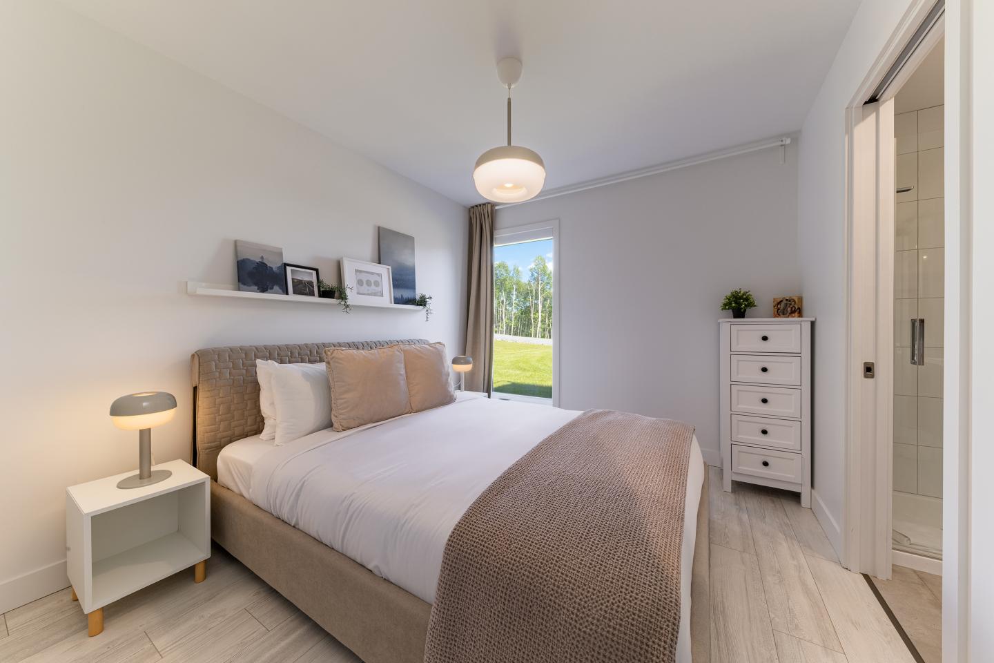 Chambre moderne avec lit double, lampe, et vue sur jardin par la fenêtre.