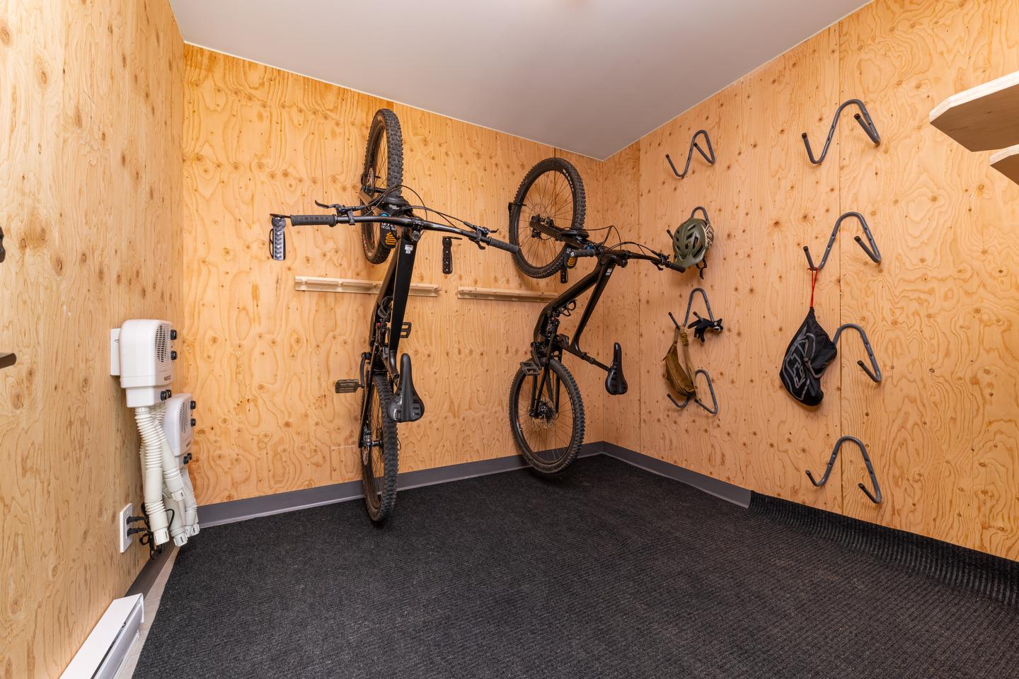 Deux vélos accrochés au mur d'une pièce en bois clair. Crochets métalliques visibles.