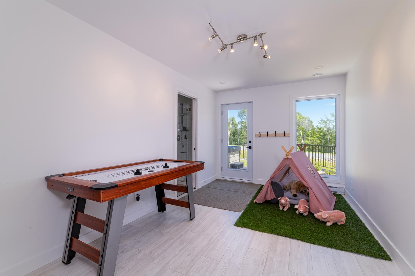 Salle de jeux lumineuse avec table de hockey et tente rose sur tapis vert.