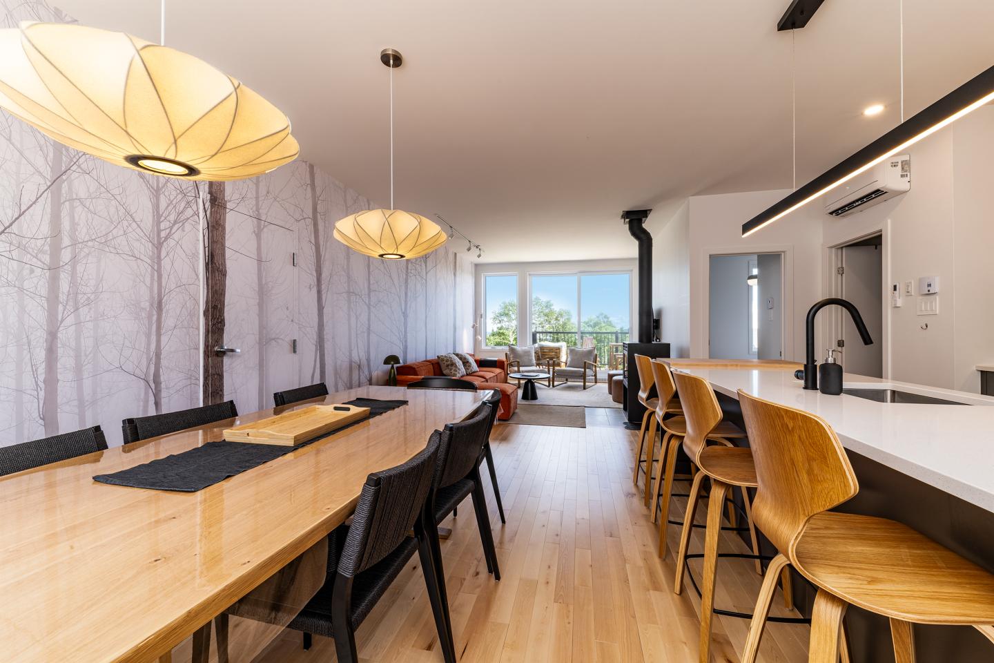 Salle à manger moderne avec table en bois, chaises noires, lumière naturelle.