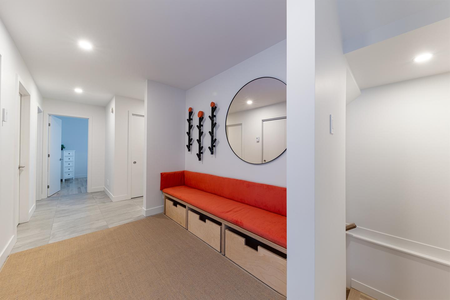 Couloir moderne avec banc rouge, miroir rond et éclairage encastré.