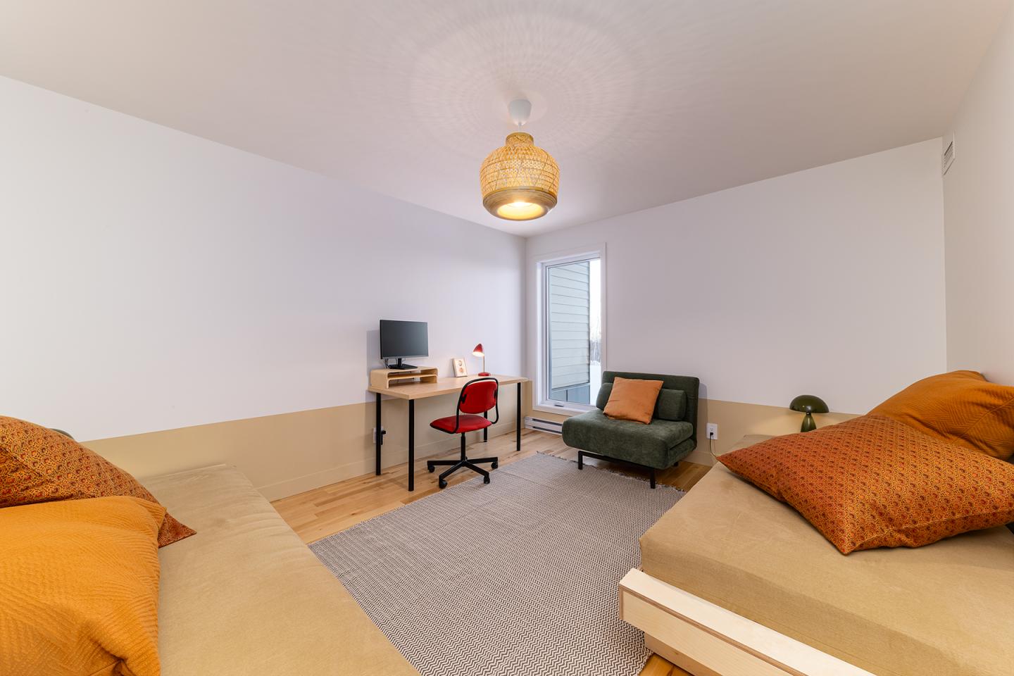 Chambre moderne avec deux lits, bureau et fauteuil, tons orange et beige.