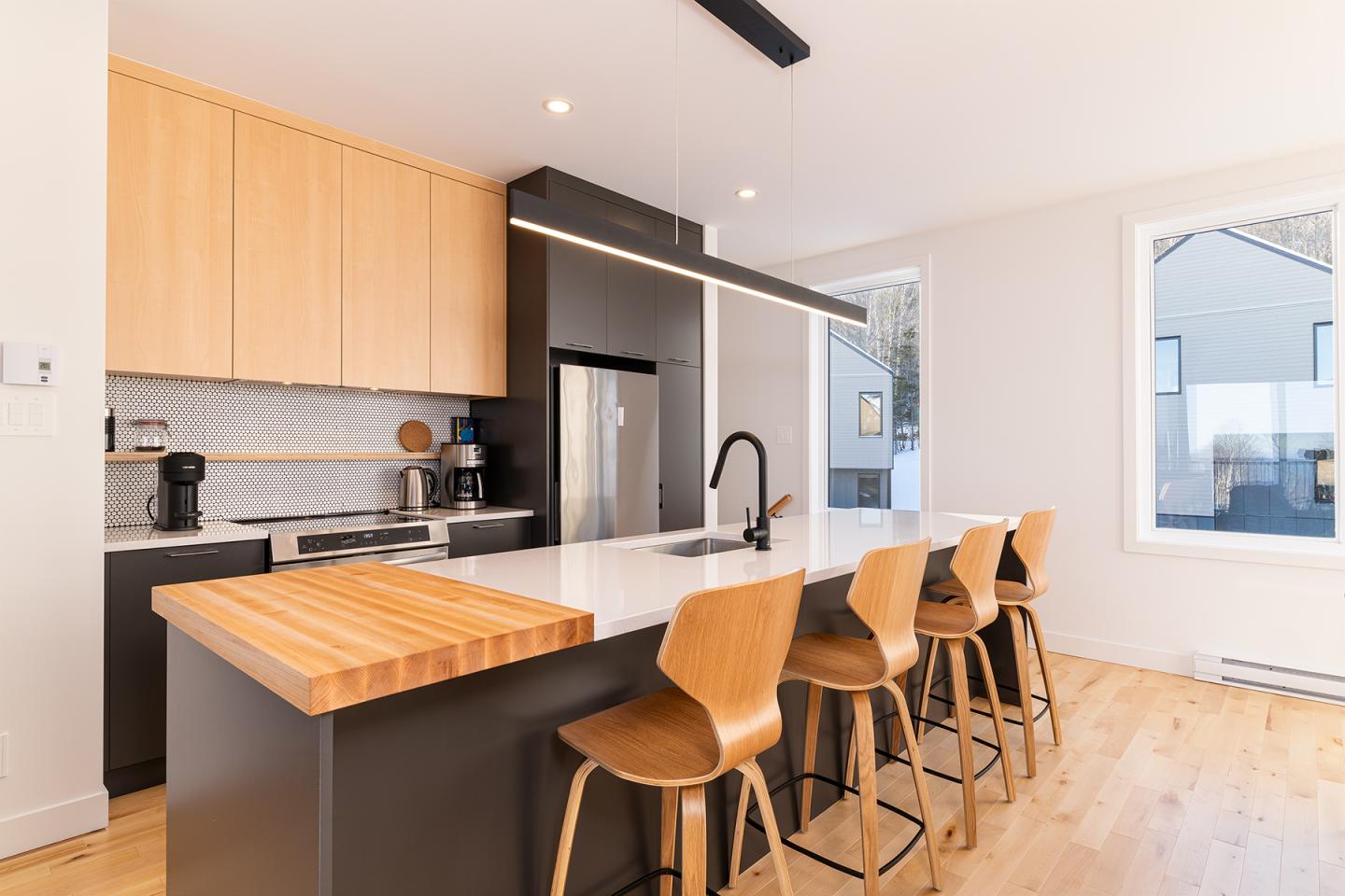 Cuisine moderne avec îlot, comptoirs en bois, chaises hautes, lumière naturelle.