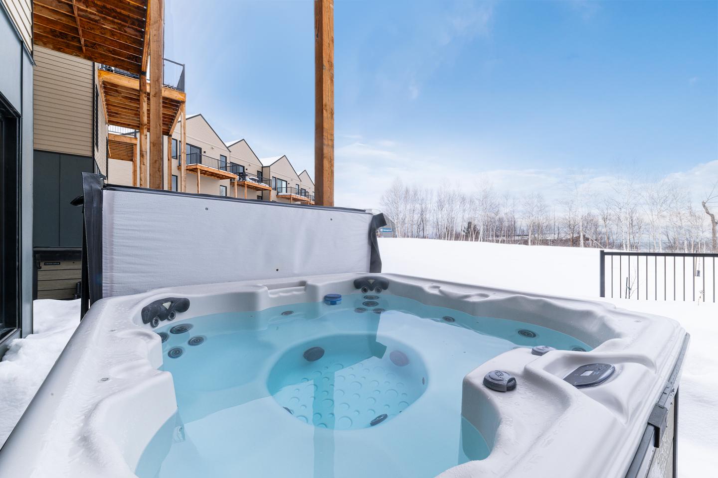Spa extérieur sous ciel bleu près d'une maison, neige autour.