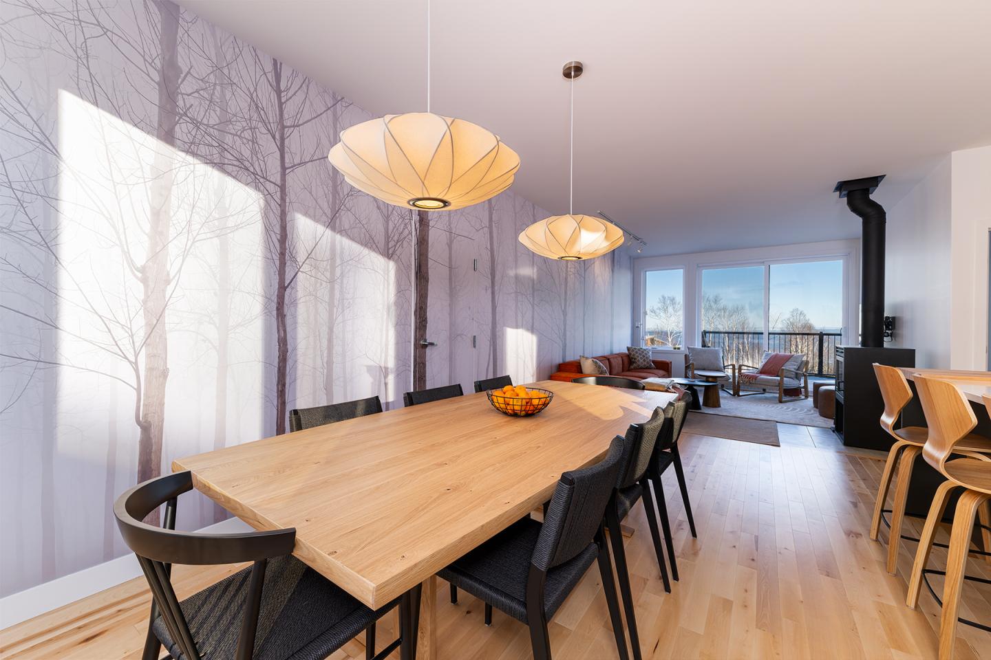 Salle à manger moderne avec table en bois, chaises noires et suspensions en forme de cloche.