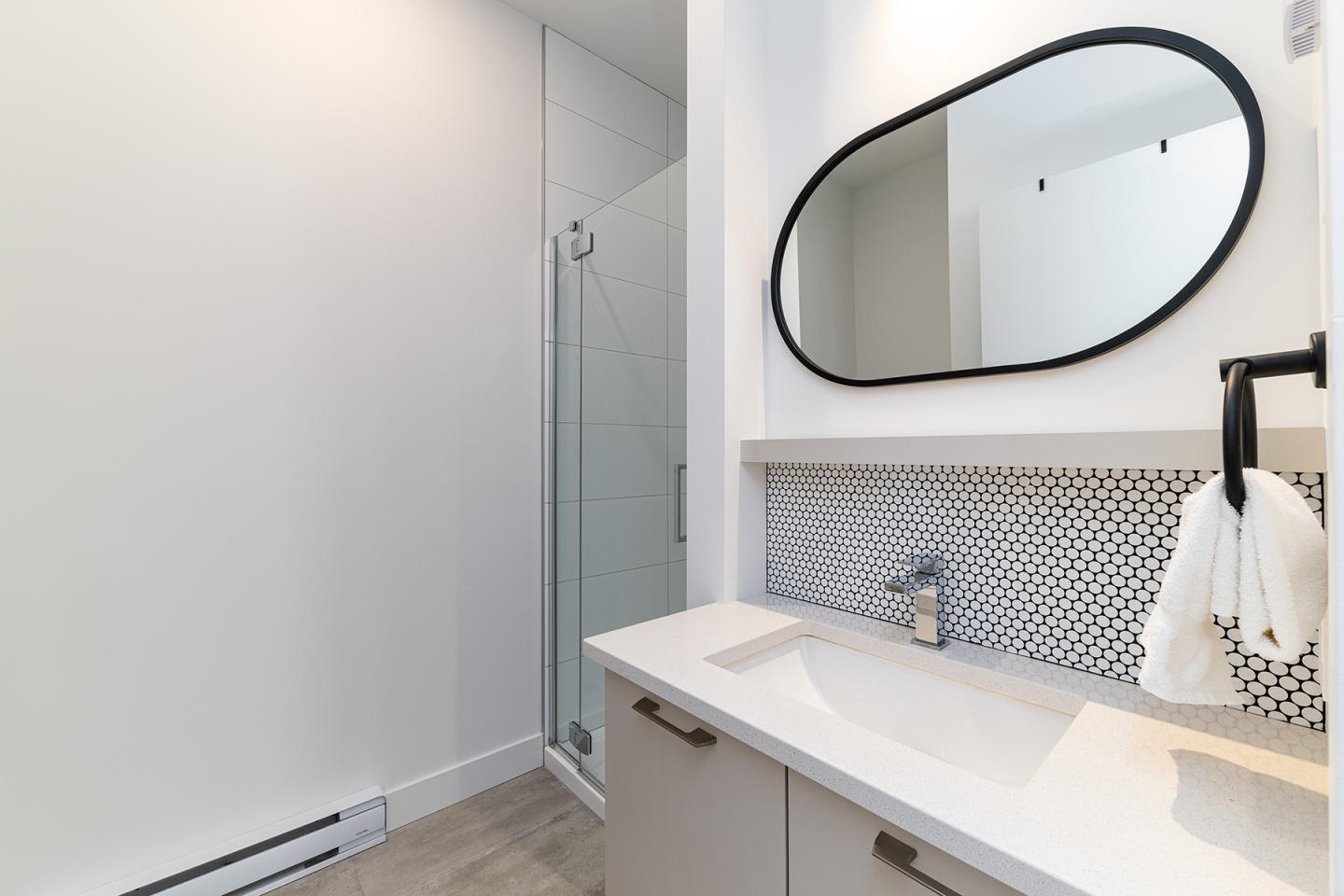 Salle de bain moderne avec lavabo blanc et miroir ovale noir. Douche à gauche.