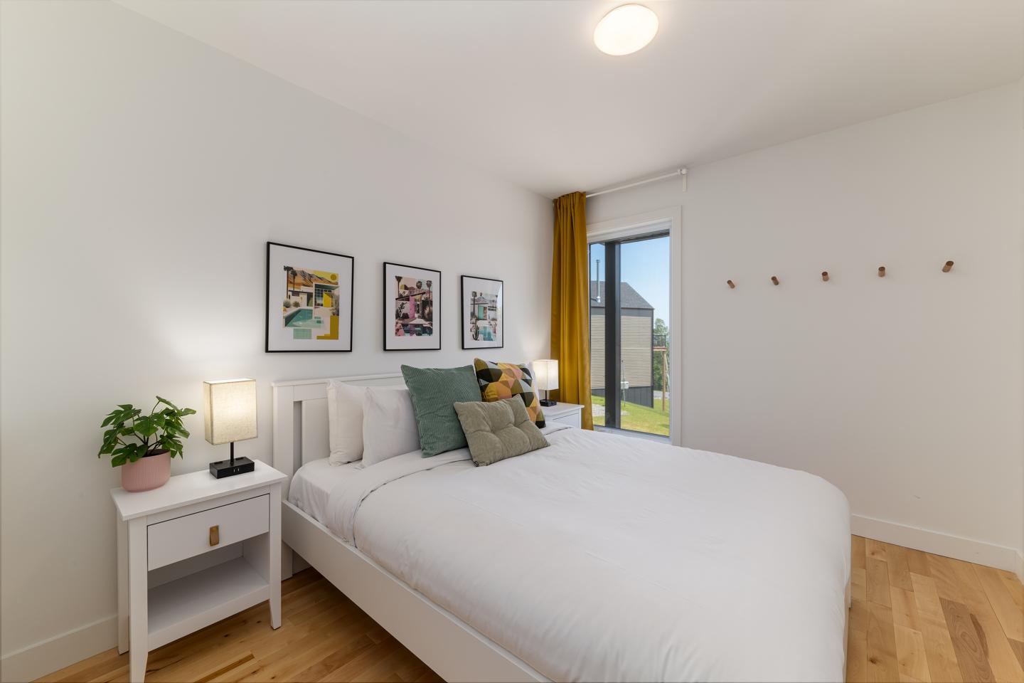 Chambre moderne avec lit blanc, coussins verts, lampes et tableaux au mur.