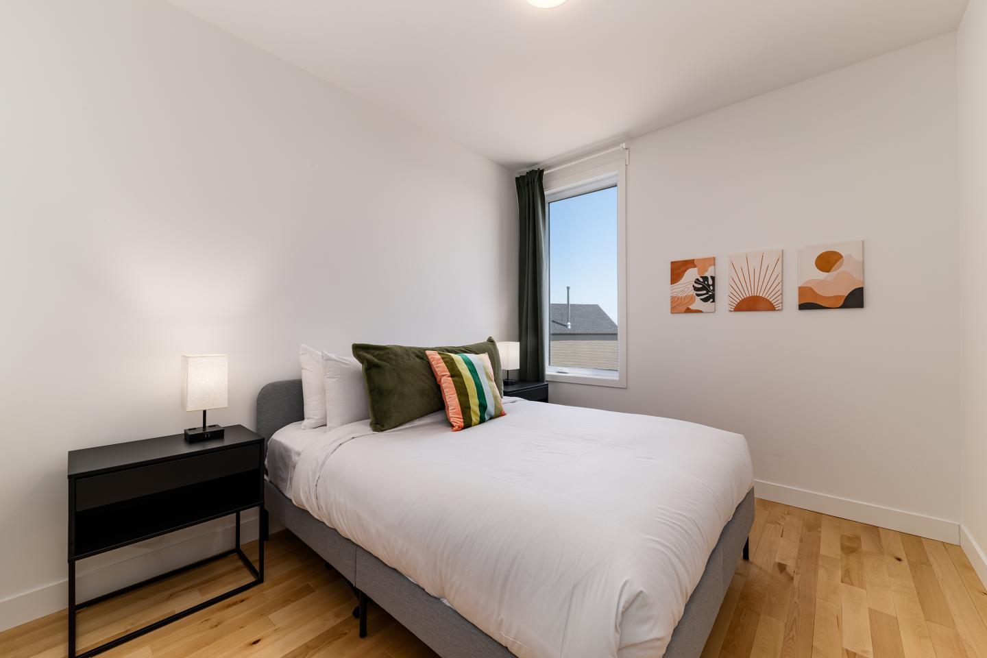 Chambre moderne avec lit, oreillers verts, et lampe sur une table de chevet.