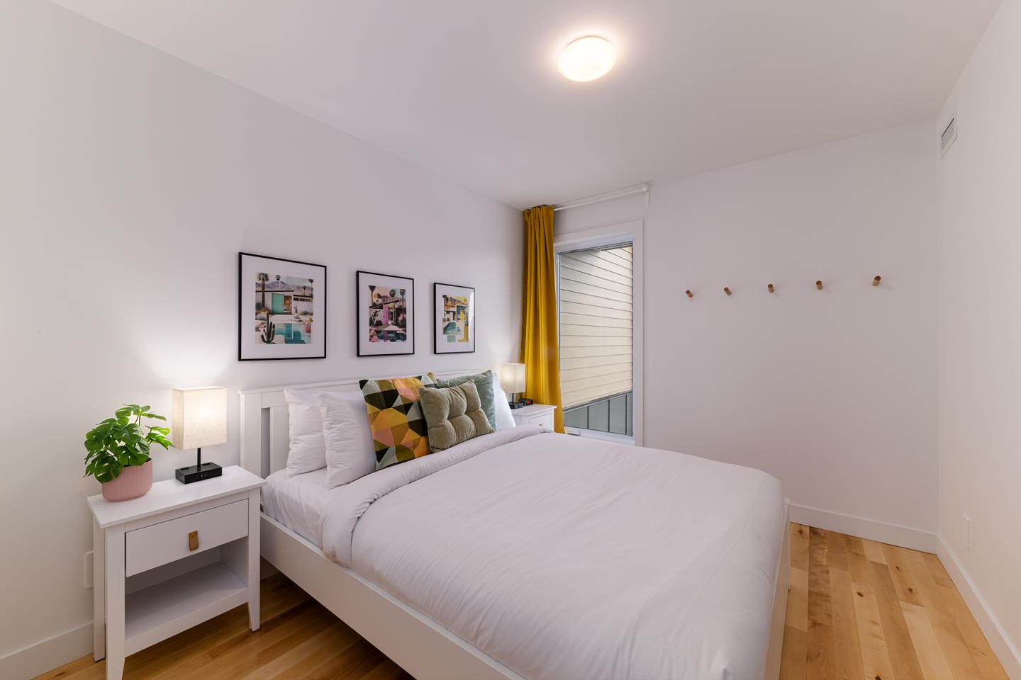 Chambre moderne avec lit, coussins colorés, et plantes sur la table de chevet.