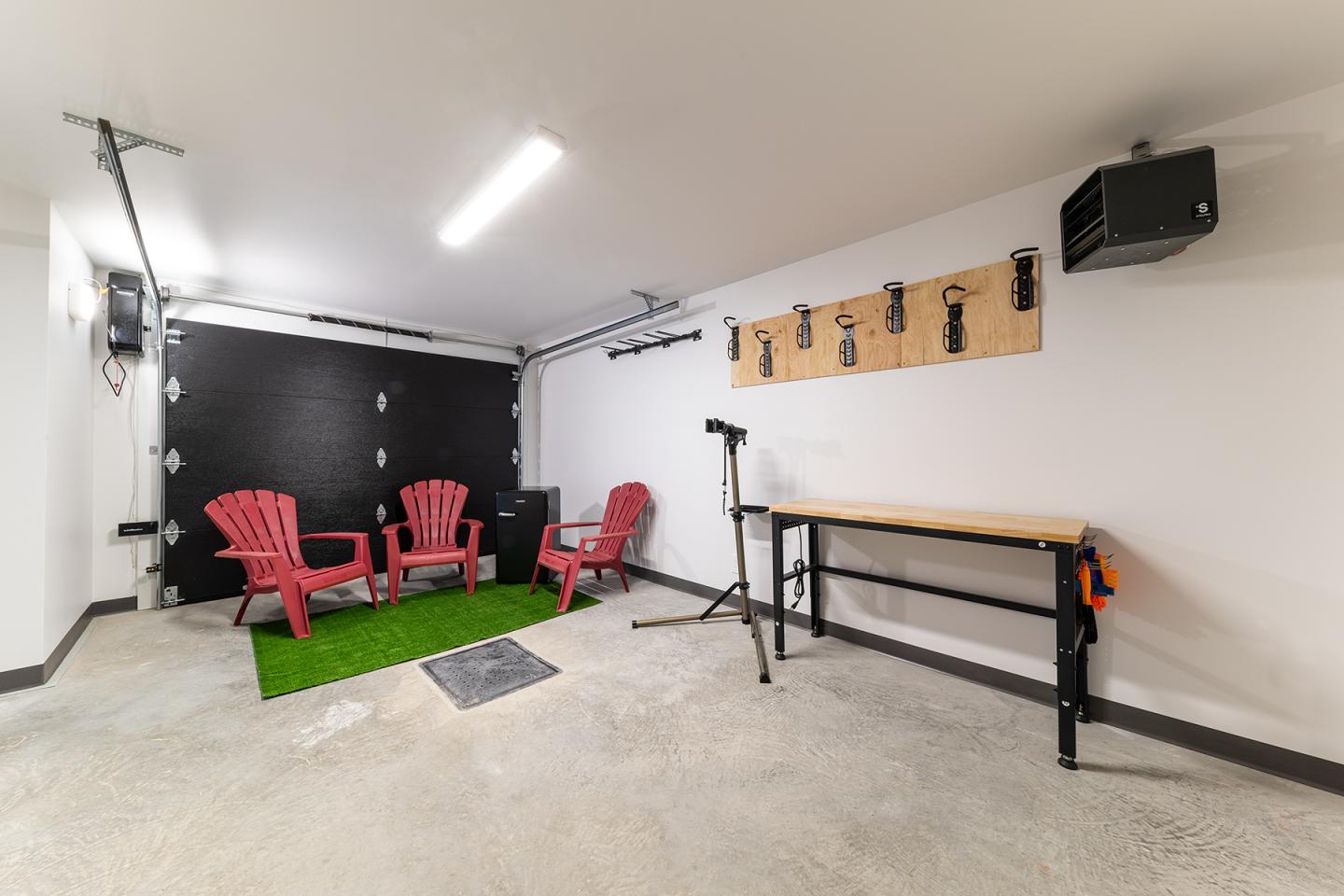 Garage avec chaises rouges, étagère murale, établi, et tapis vert.