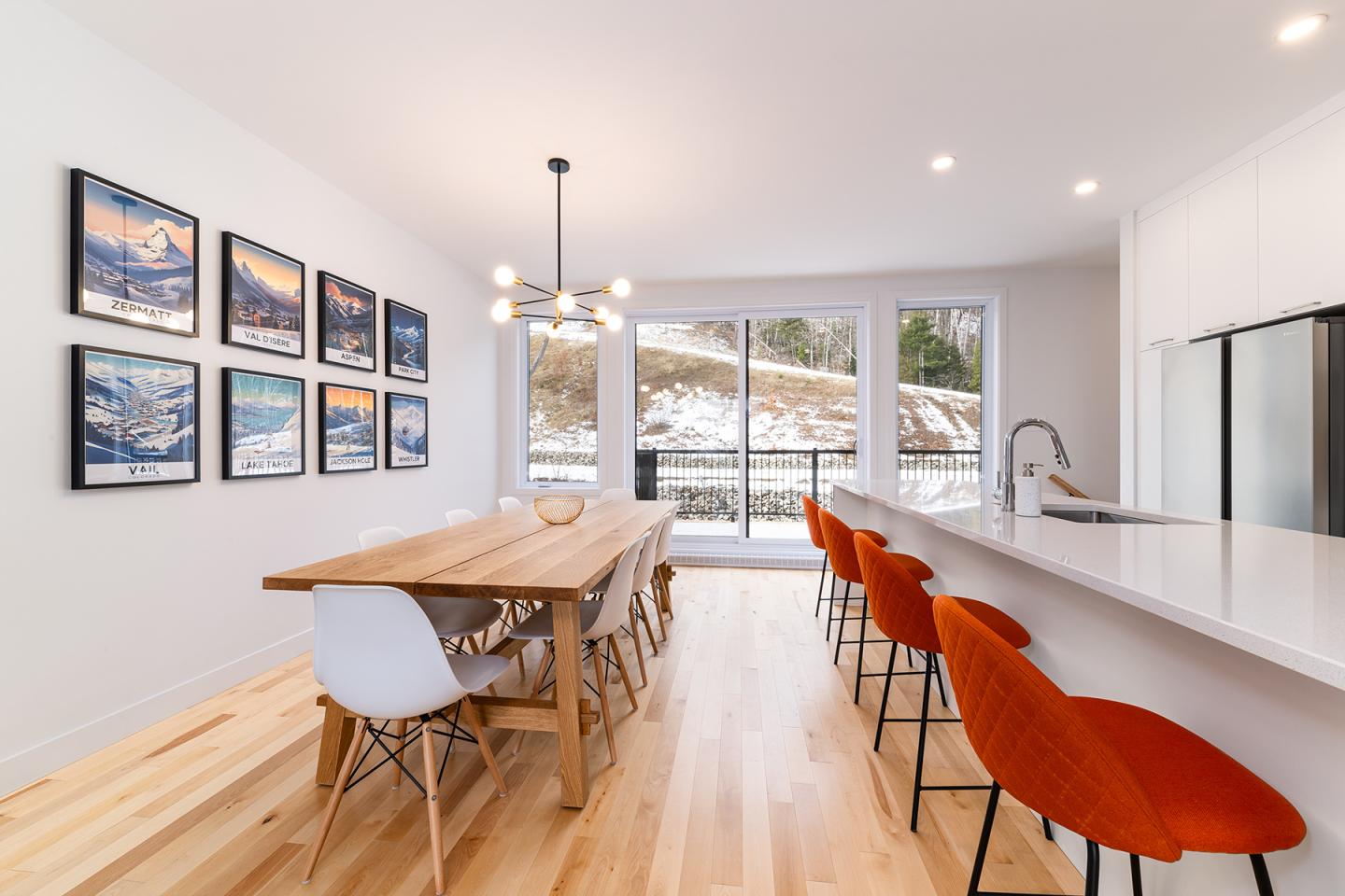 Salle à manger moderne avec table en bois, chaises orange et grandes fenêtres.