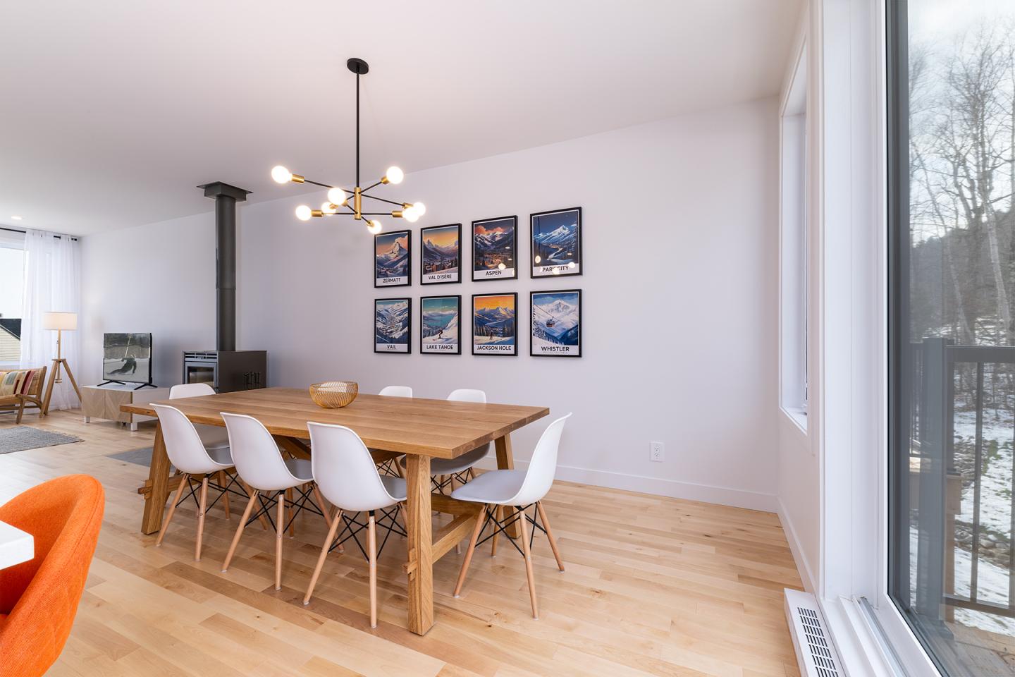 Salle à manger lumineuse avec table bois, chaises blanches, et œuvres sur le mur.