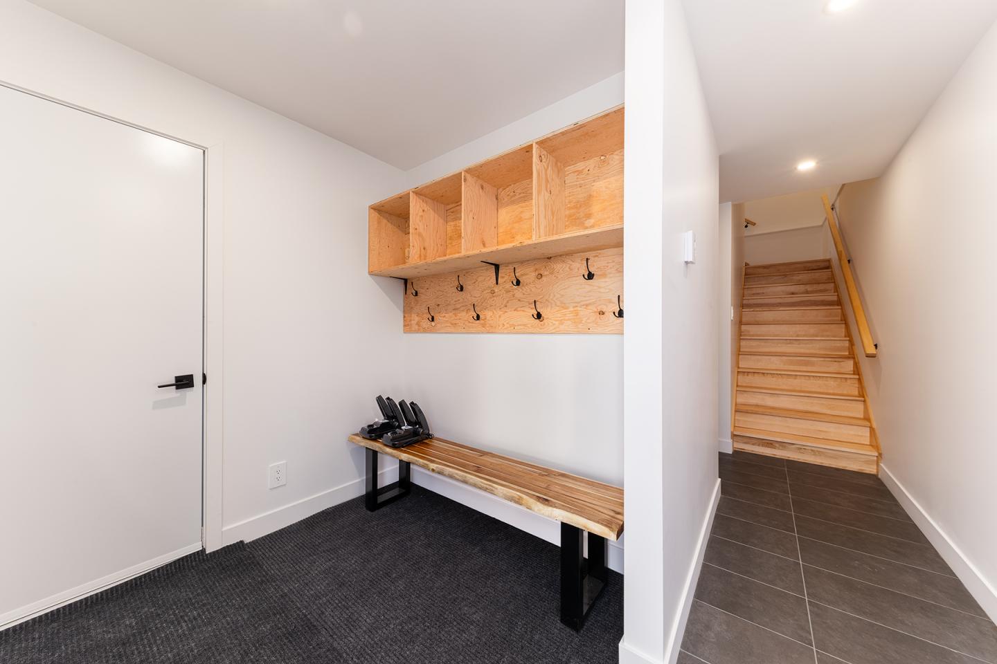 Couloir moderne avec étagères en bois, banc, escaliers en bois à droite.