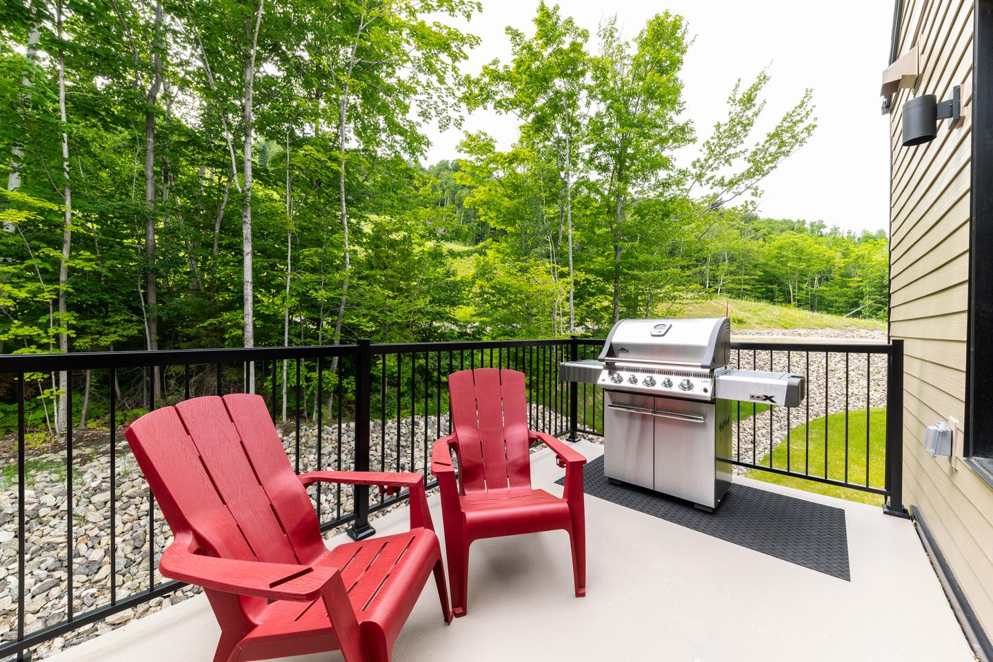 Deux chaises rouges et un barbecue sur une terrasse boisée.