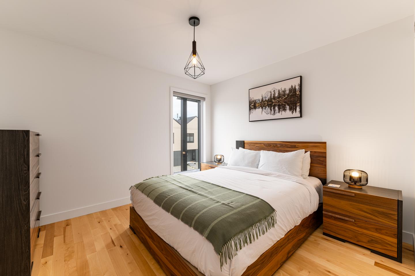 Chambre moderne avec lit double, couvre-lit vert, tableau de forêt au mur.