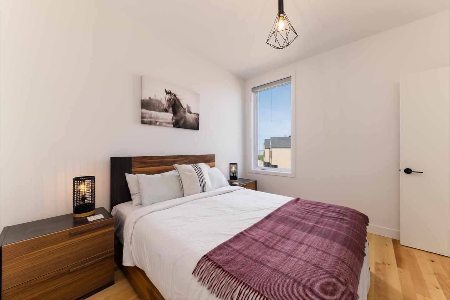 Chambre moderne, lit double, lampes de chevet, fenêtre ensoleillée.