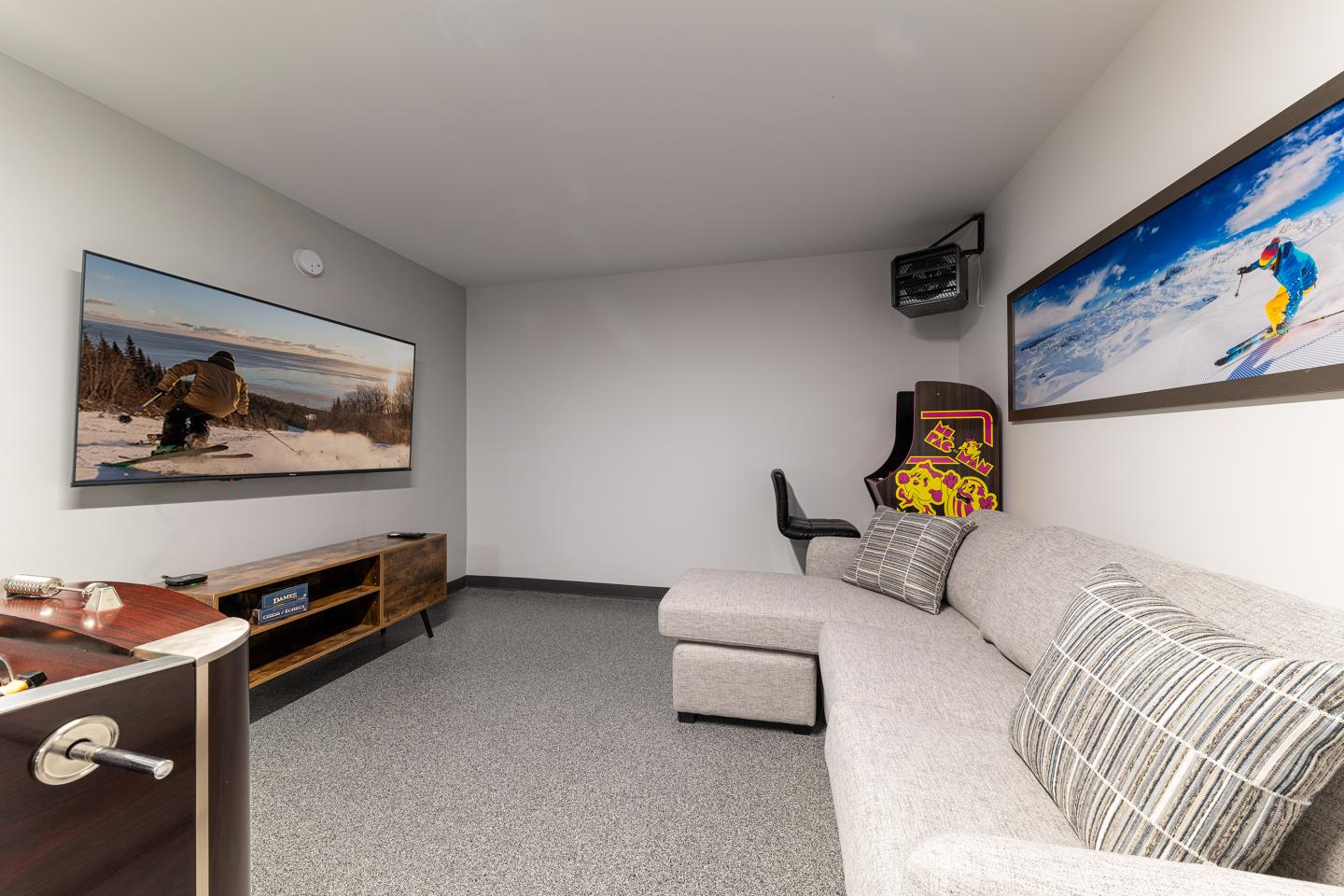 Salle de jeux avec canapé, flipper, et deux grandes photos.