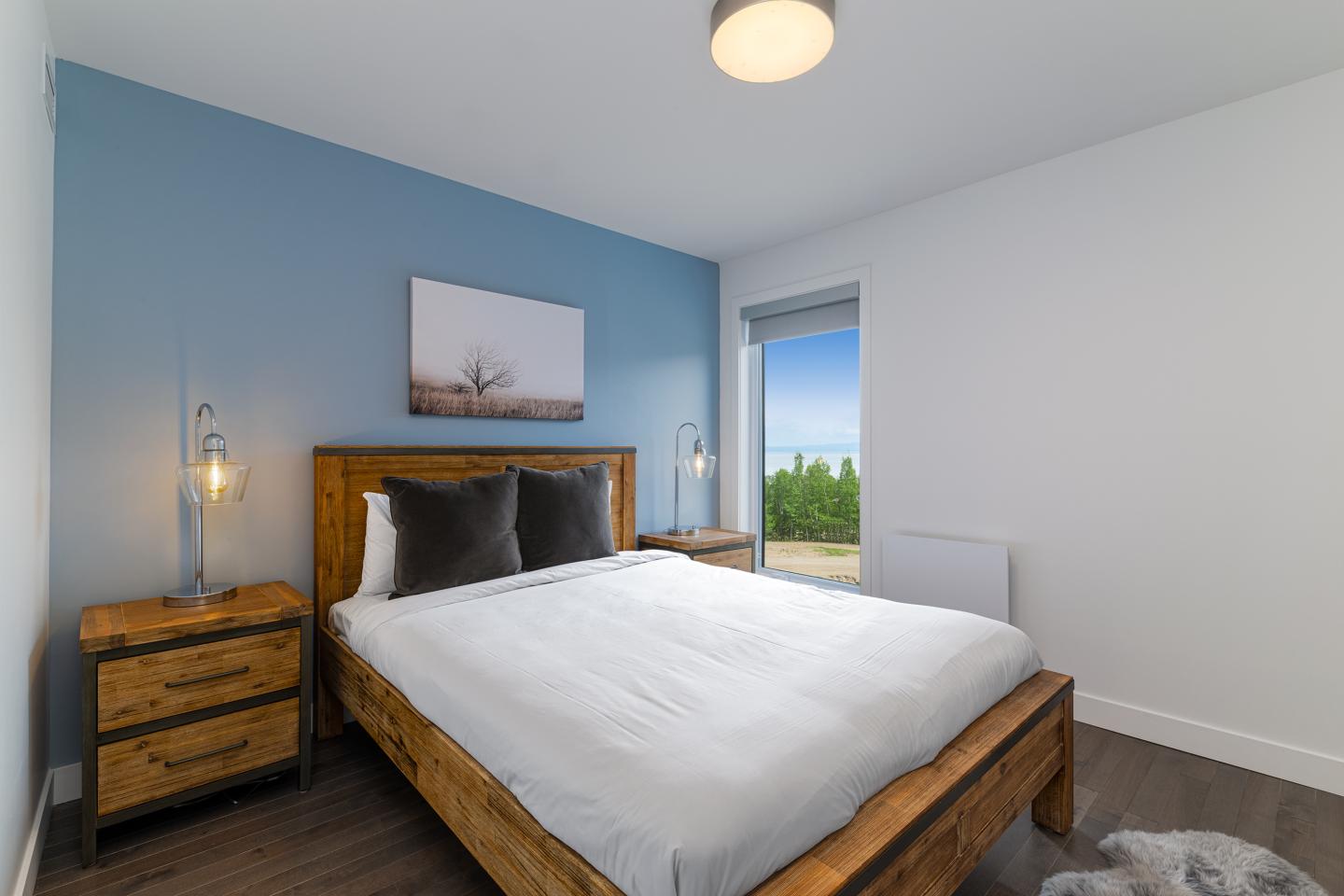 Chambre moderne avec mur bleu, lit en bois, grandes fenêtres.