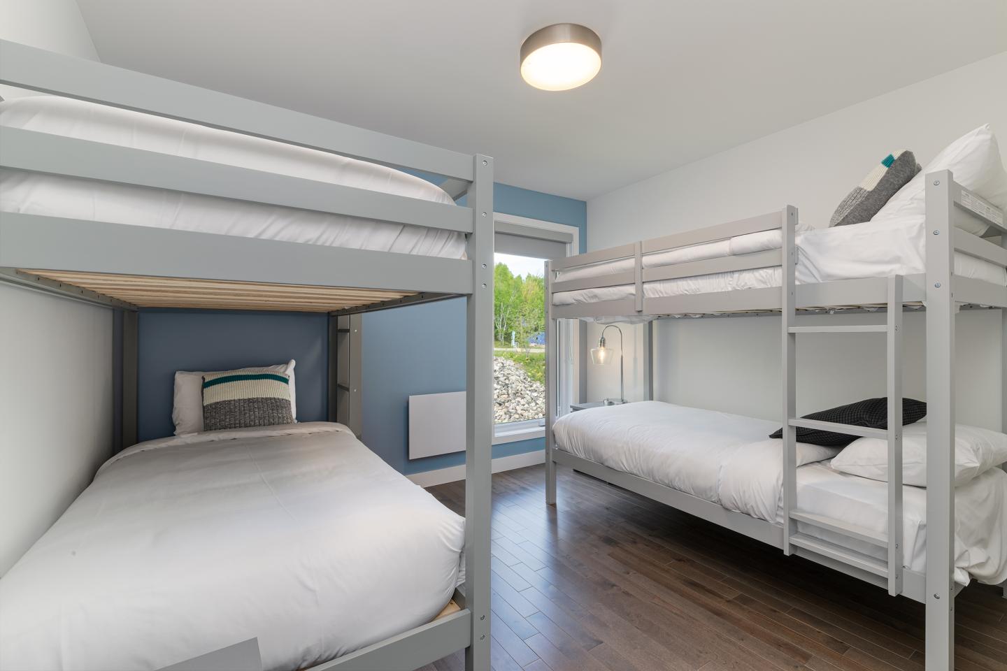 Chambre avec lits superposés, murs blancs et fenêtre lumineuse.