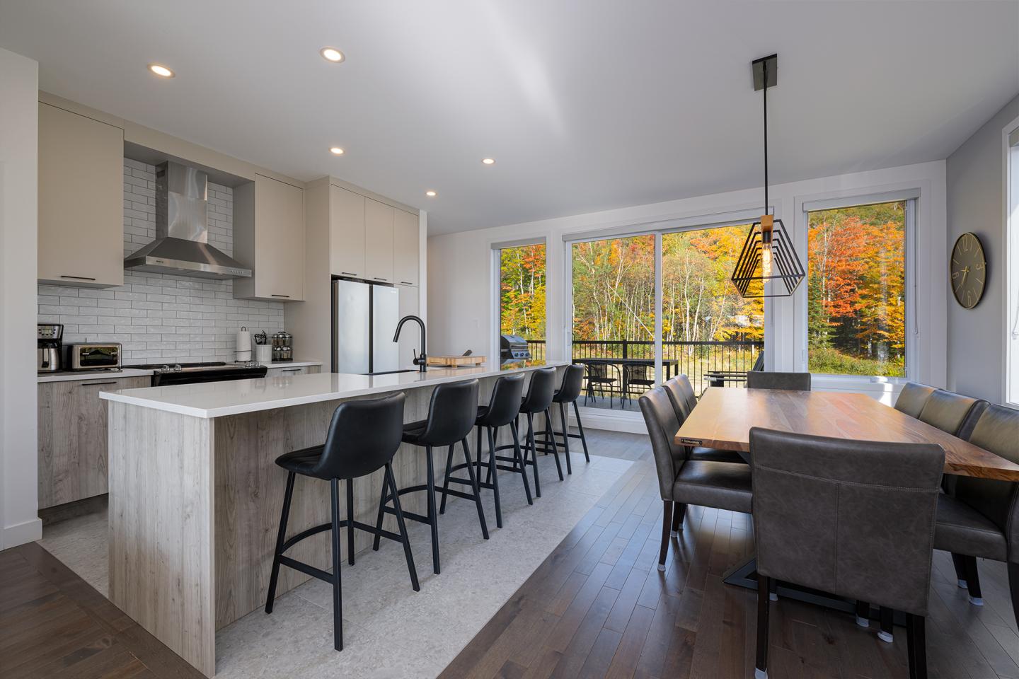 Cuisine moderne avec îlot central et chaises, salle à manger avec vue sur jardin d'automne.
