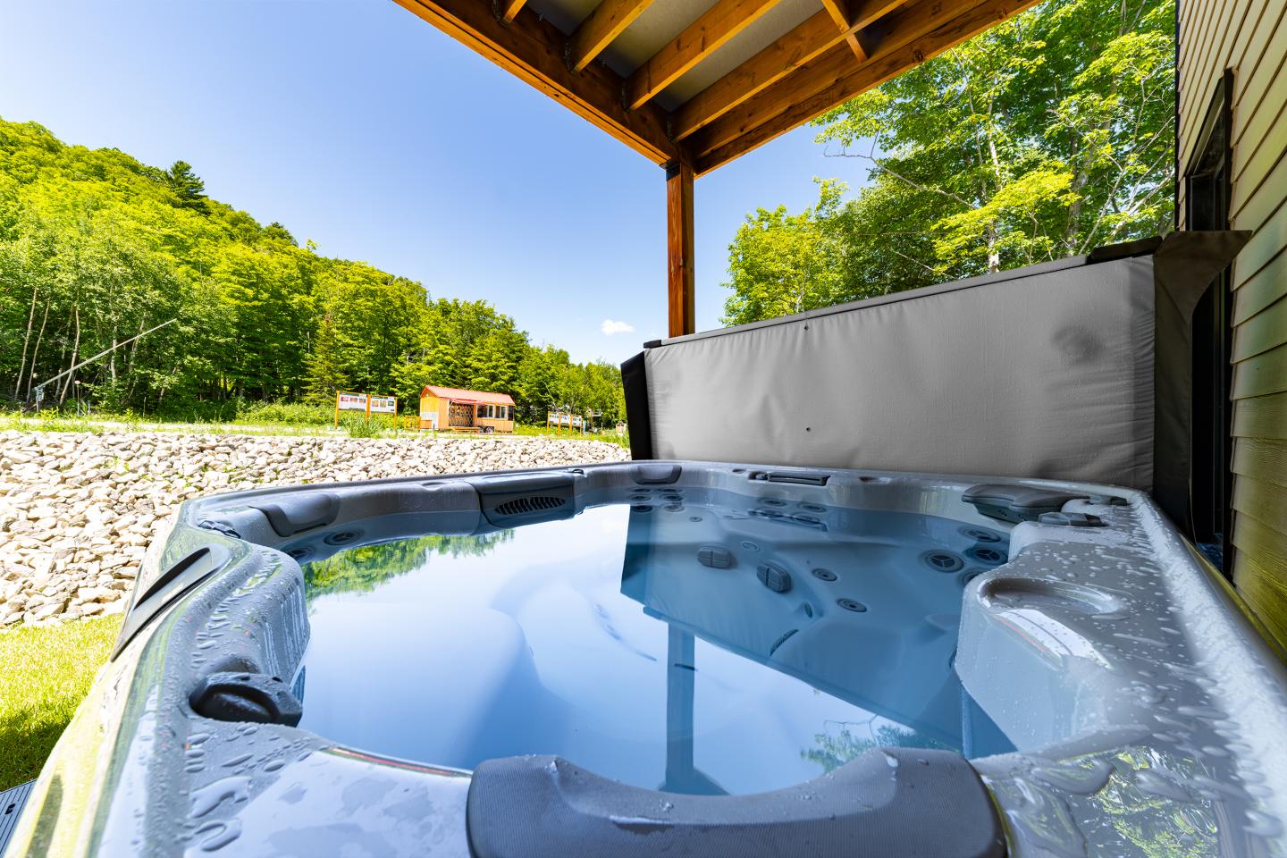 Spa extérieur entouré de verdure sous un auvent en bois.