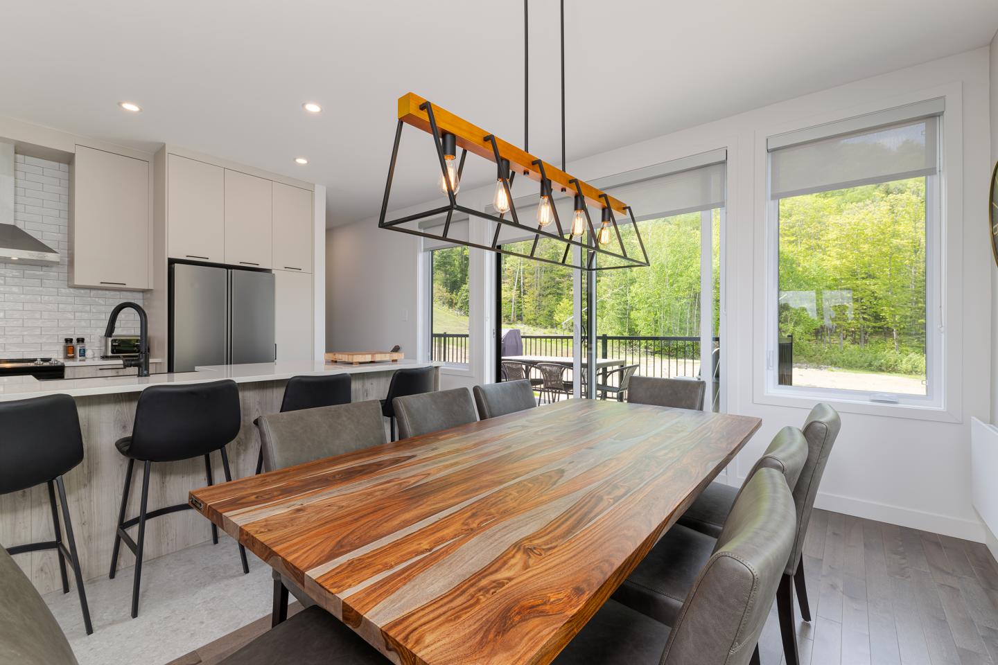 Salle à manger moderne avec grande table en bois, chaises grises et lampe suspendue.